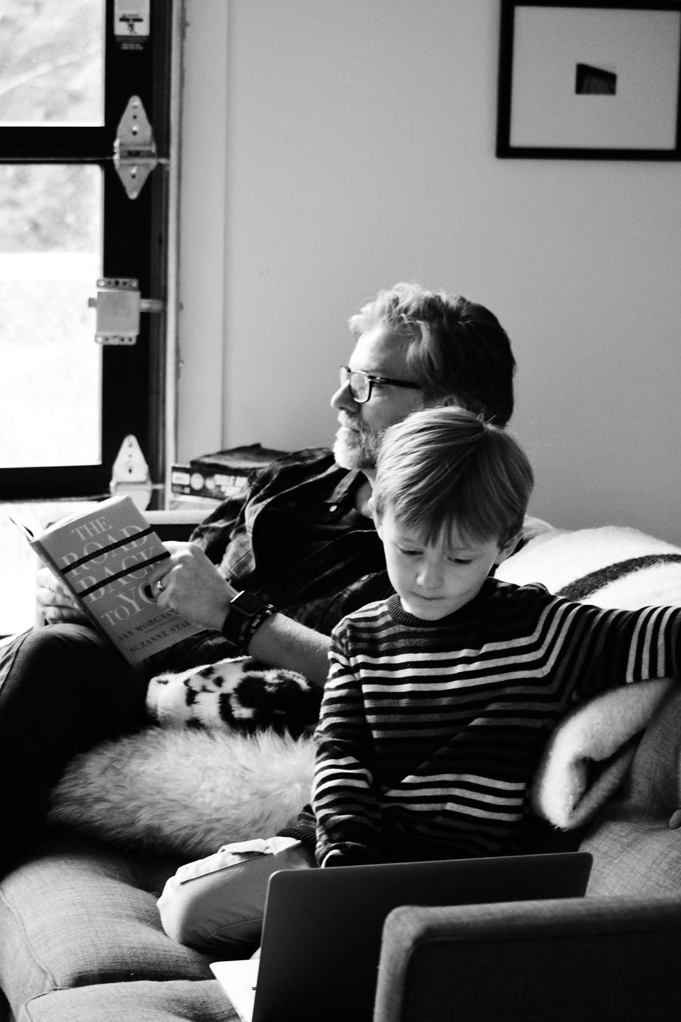 A black and white photo of a man and a boy sitting on a couch.