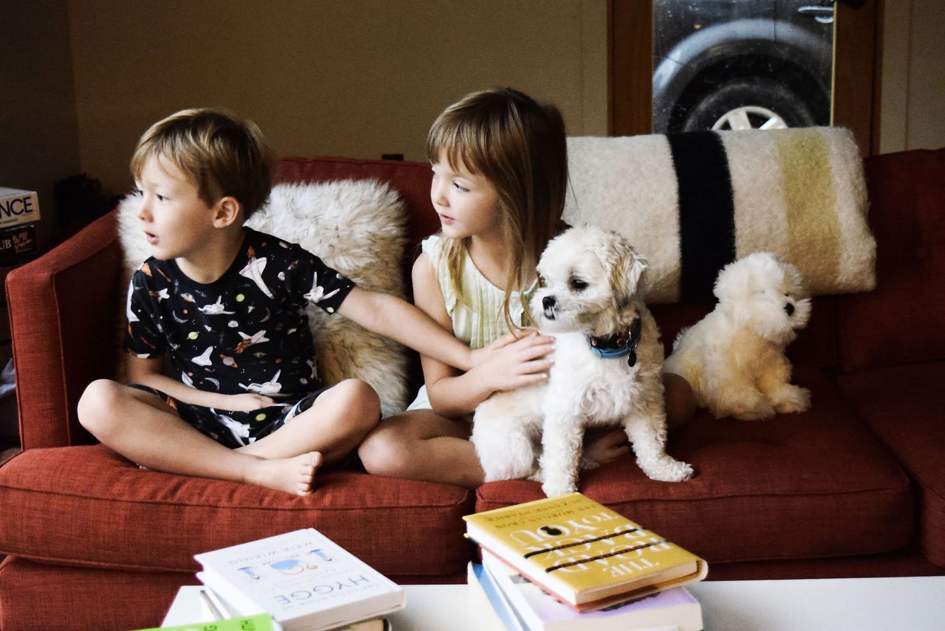 A boy and a girl are sitting on a couch with a puppy.