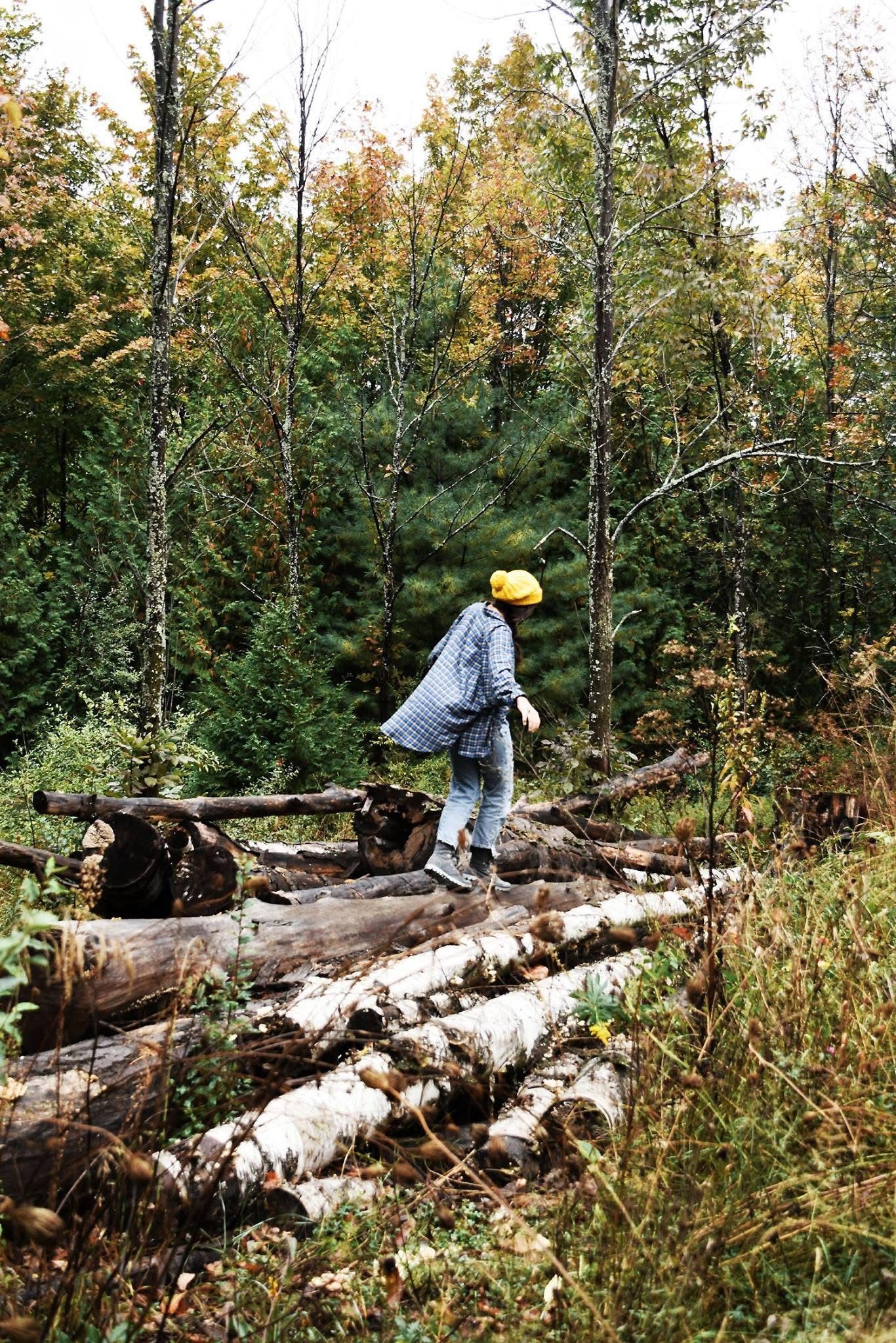 A person is walking across a pile of logs in the woods.