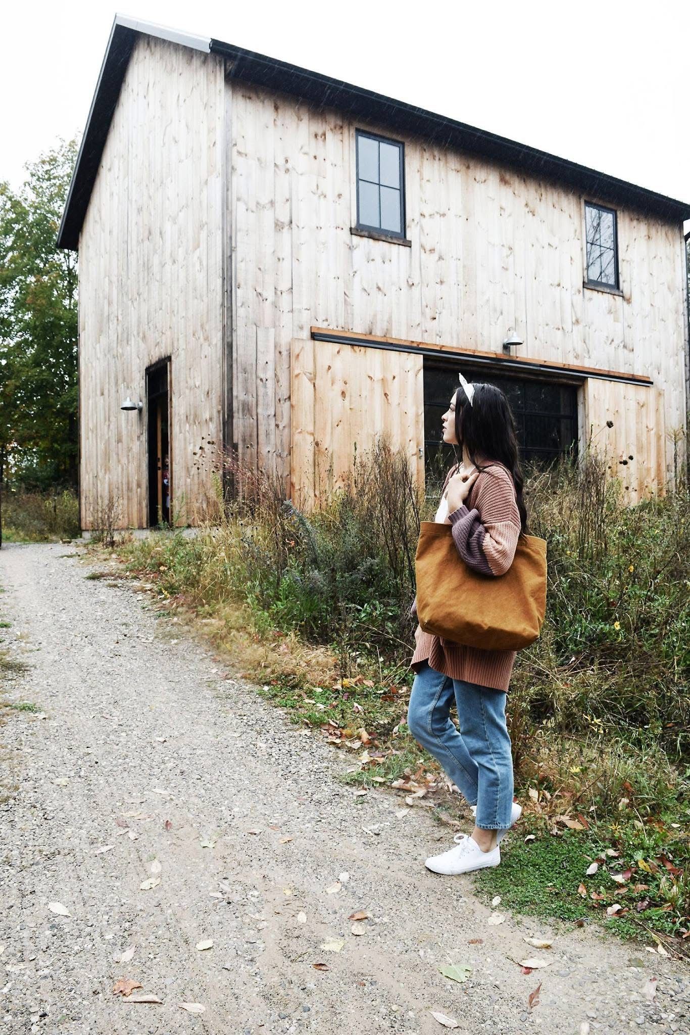 A woman is standing on a dirt road in front of a wooden house.