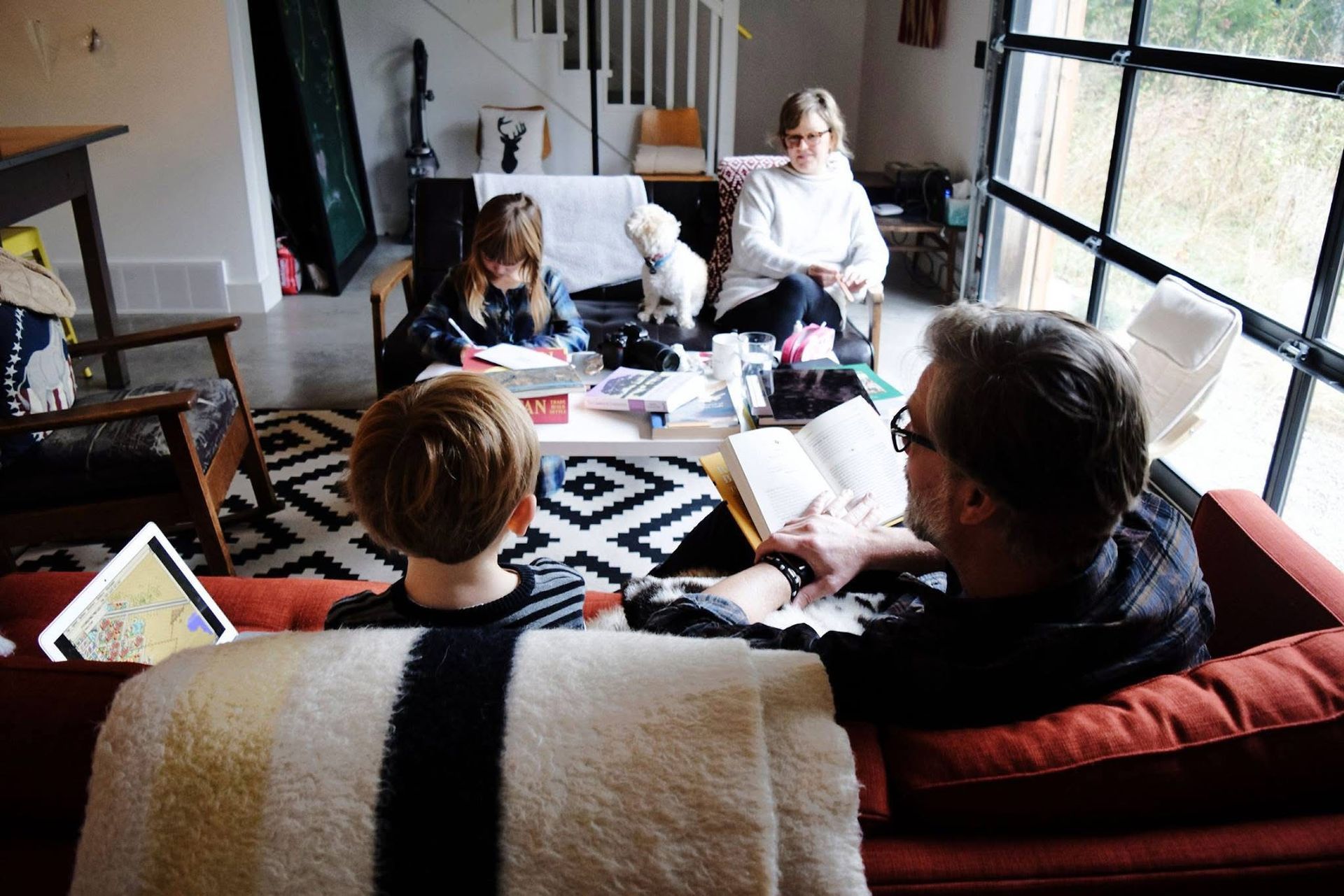 A family is sitting on a couch in a living room reading books.