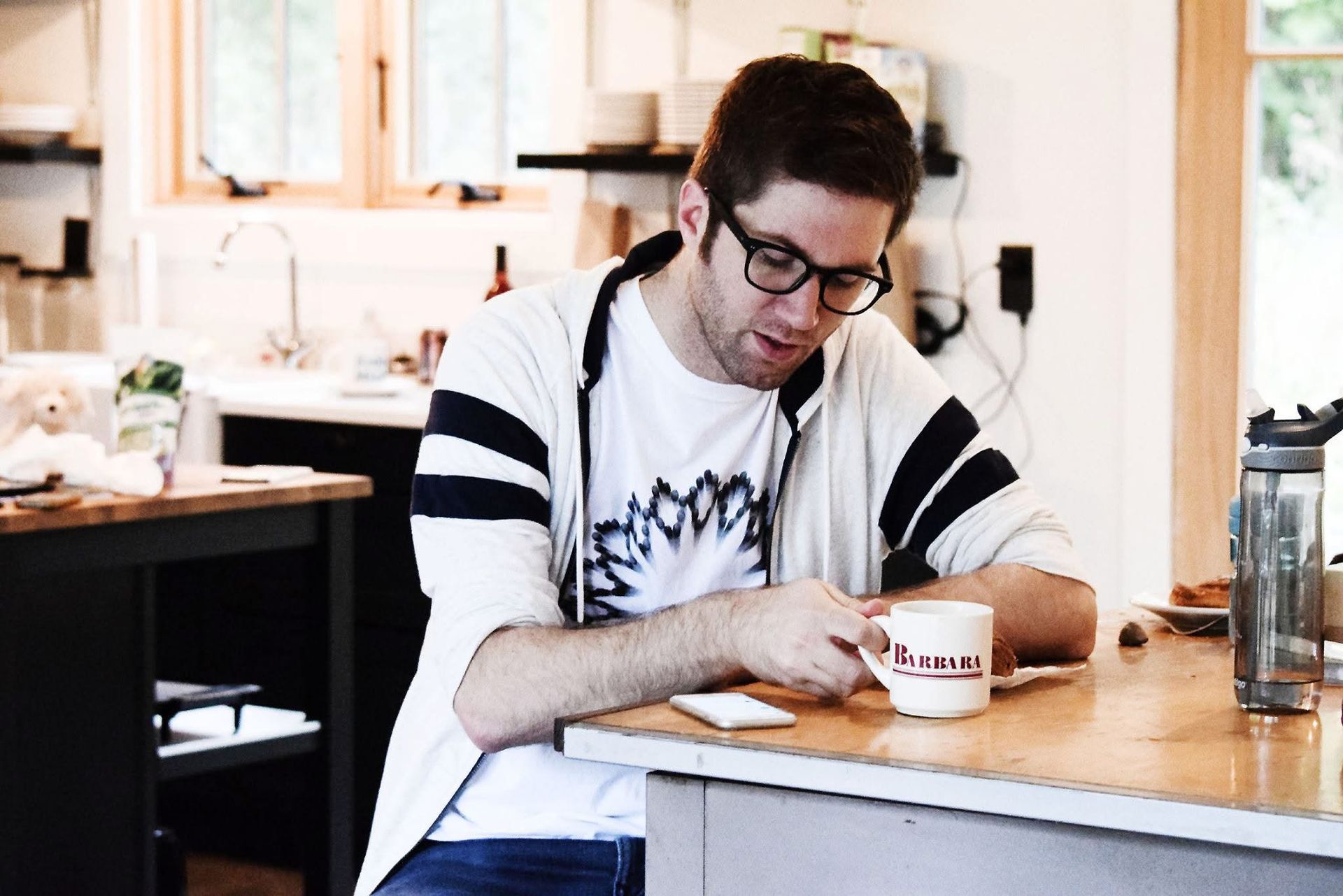 A man wearing glasses is sitting at a counter with a cup of coffee.