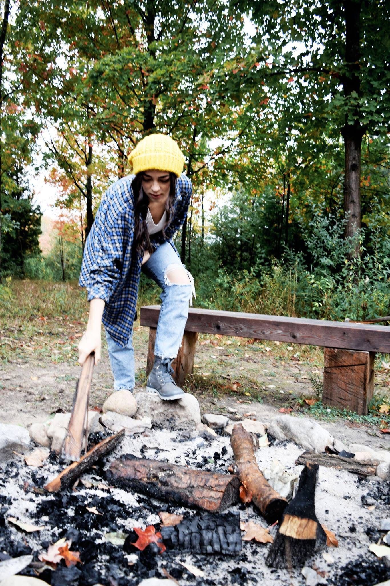 A woman is standing next to a campfire in the woods.