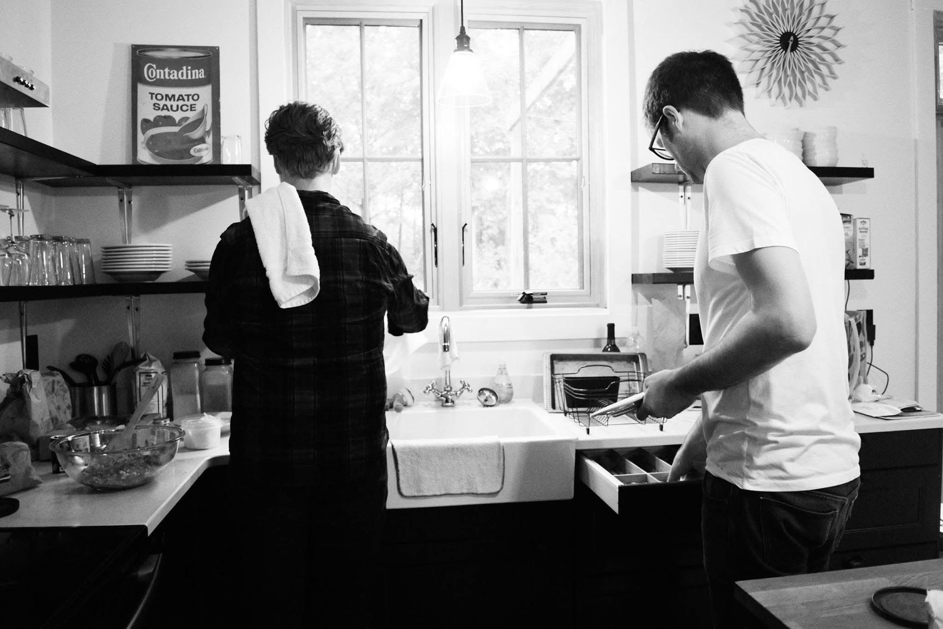 A black and white photo of two people in a kitchen.