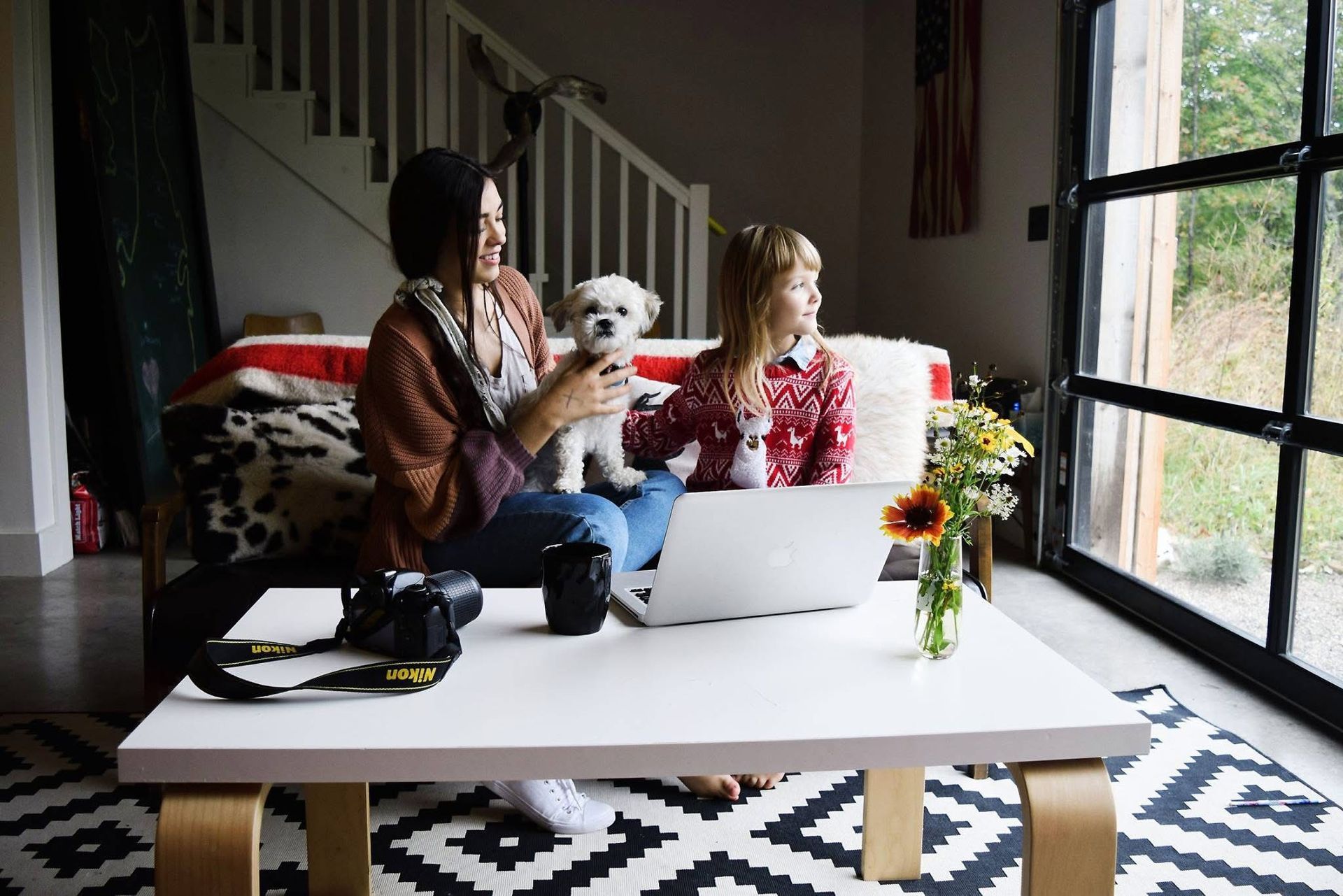 Two women are sitting on a couch with a dog and a laptop.