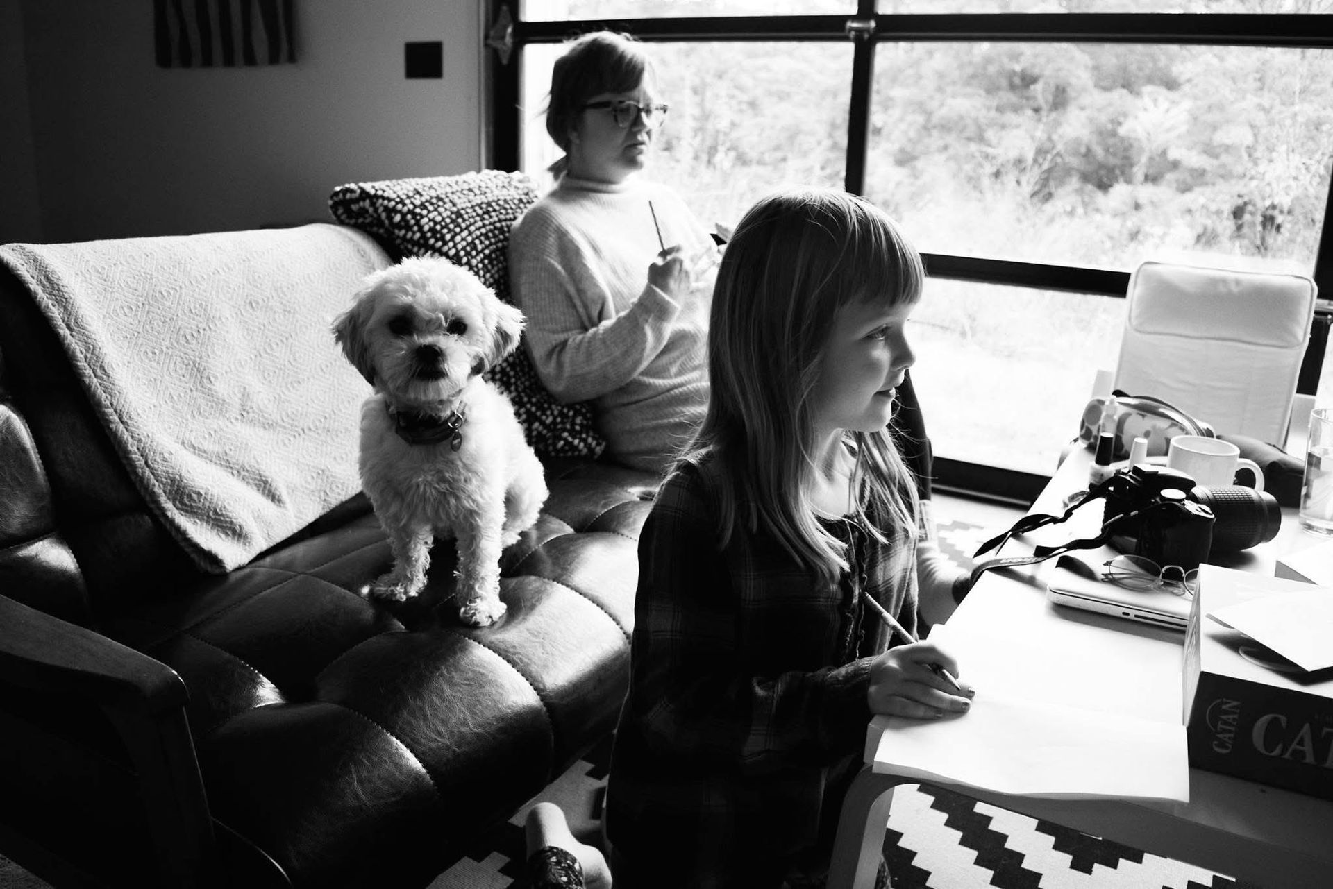 A black and white photo of a girl sitting on a couch with a dog.