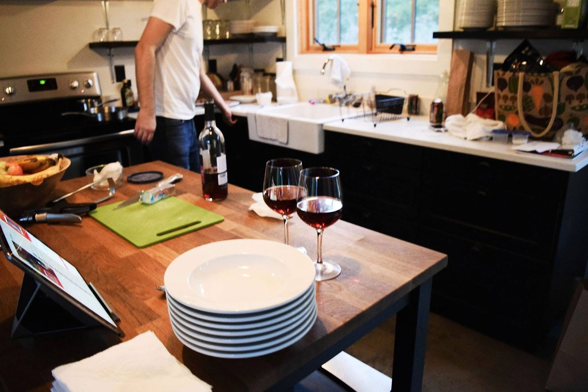 A man is standing in a kitchen next to a table with plates and wine glasses on it.