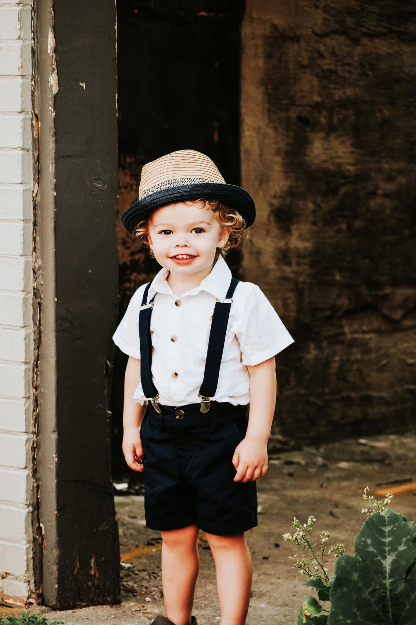 A little boy wearing suspenders and a hat