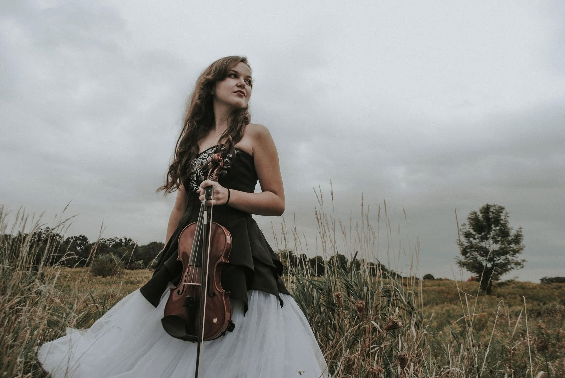 A woman in a black and white dress is holding a violin in a field.