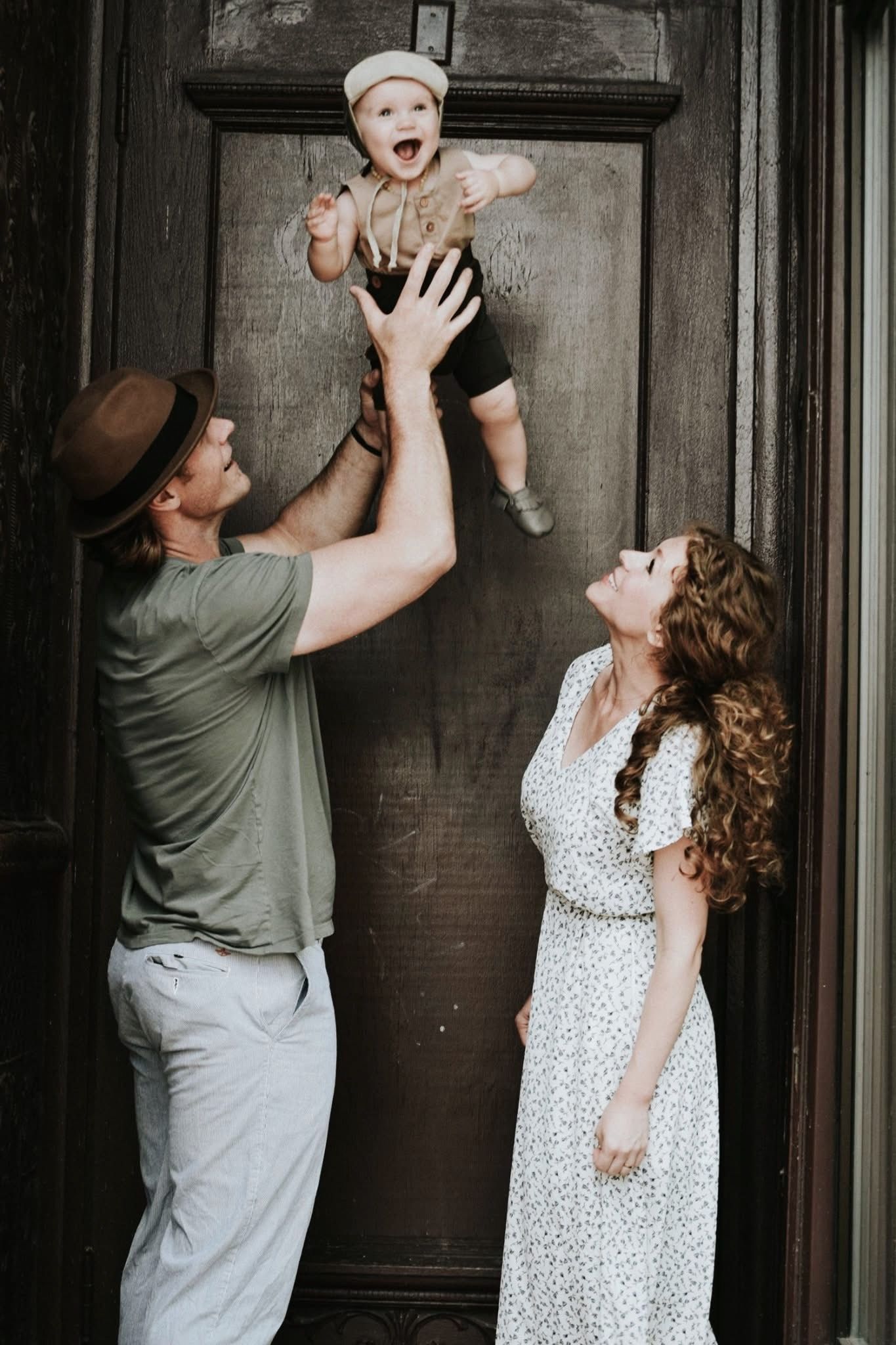 A man and woman are holding a baby in front of a door.
