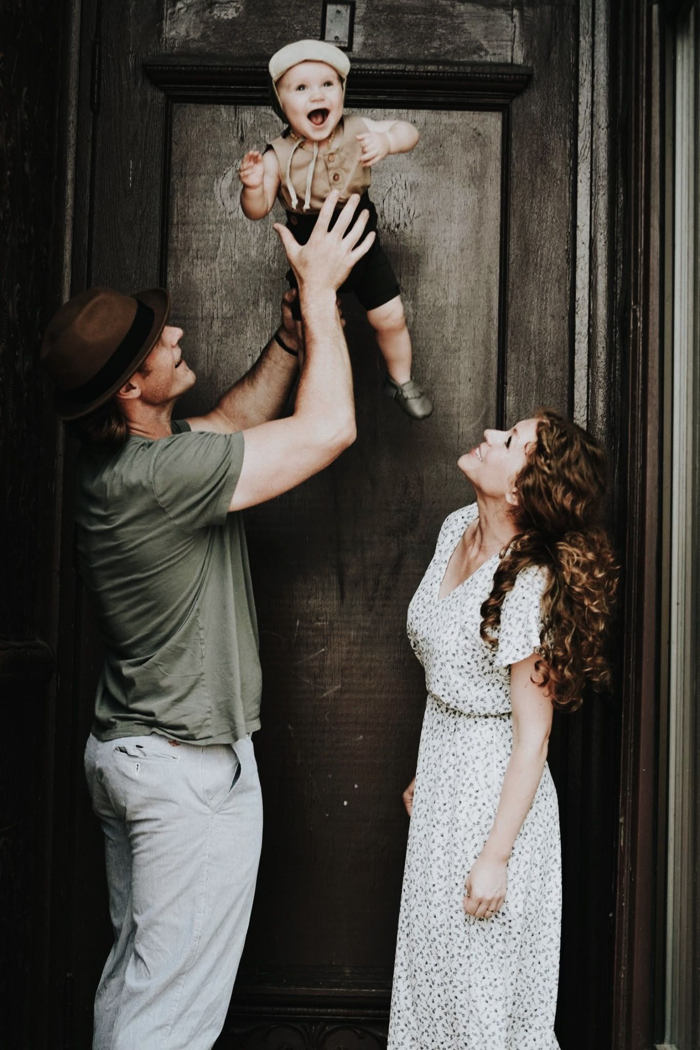 A man is holding a baby in the air while a woman looks on.