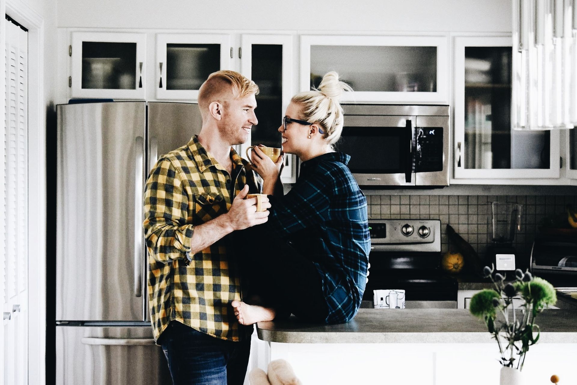 A man and a woman are standing in a kitchen drinking coffee.