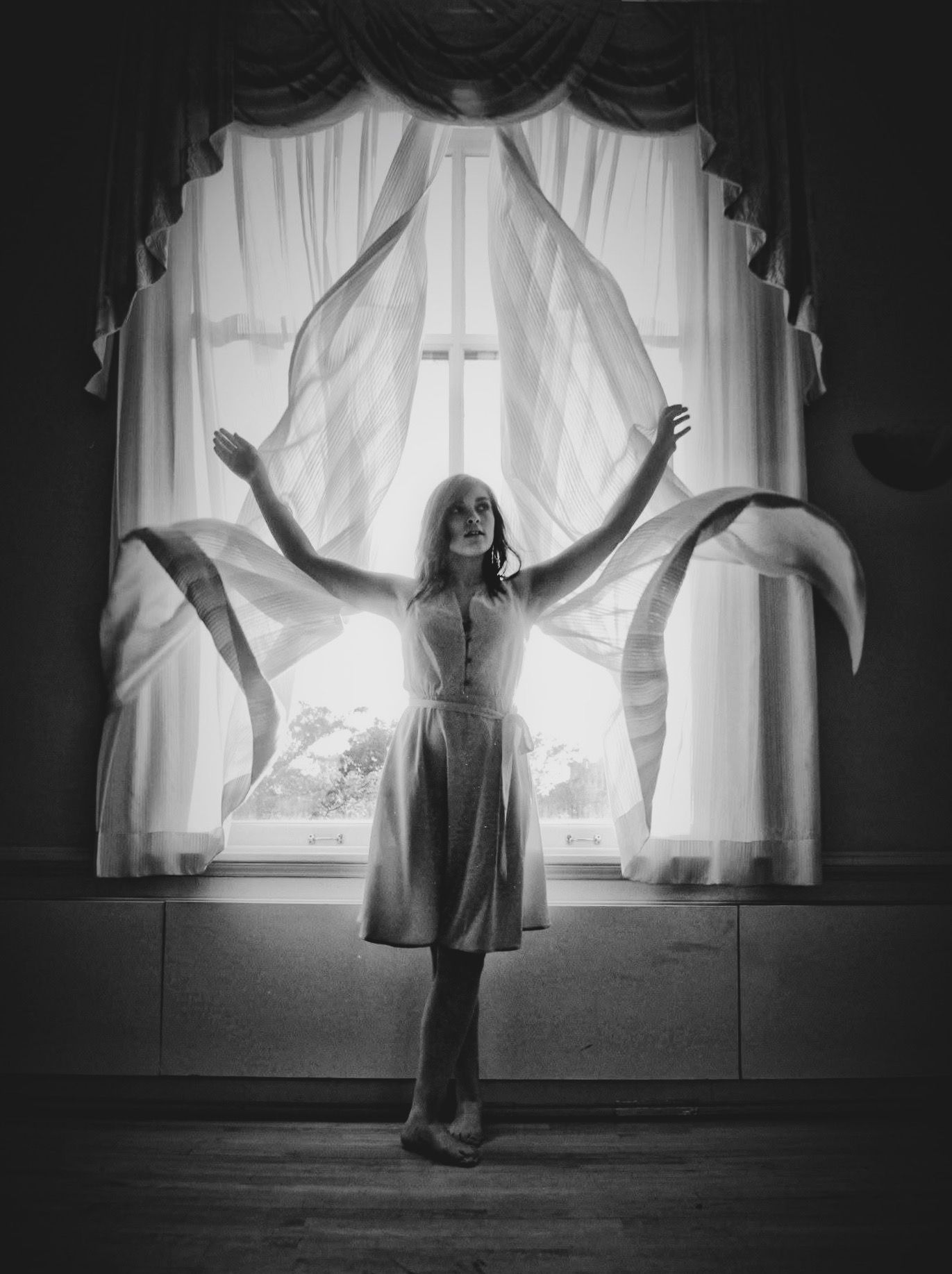 A woman is standing in front of a window with her arms outstretched.