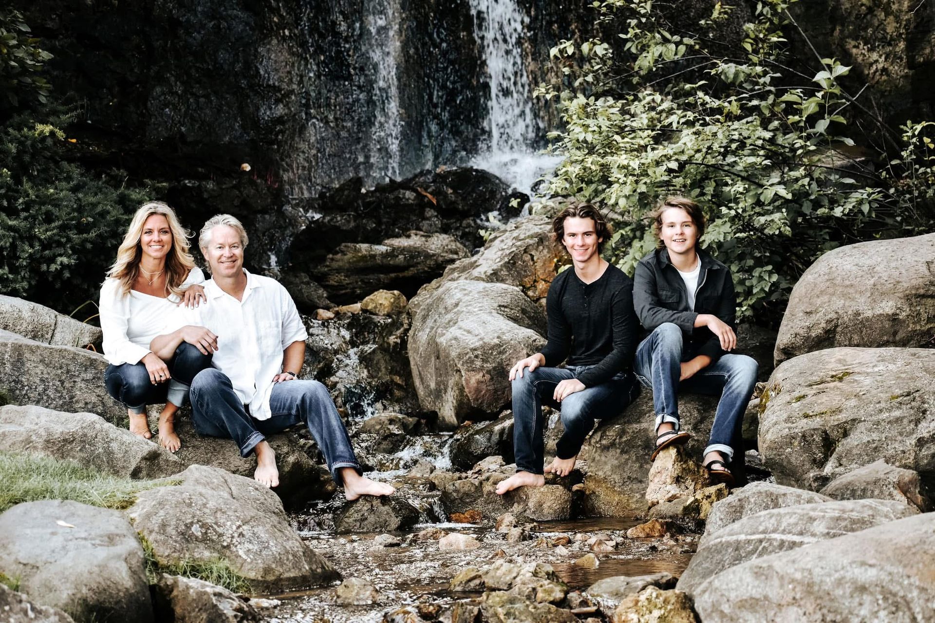 A family is sitting on rocks in front of a waterfall.