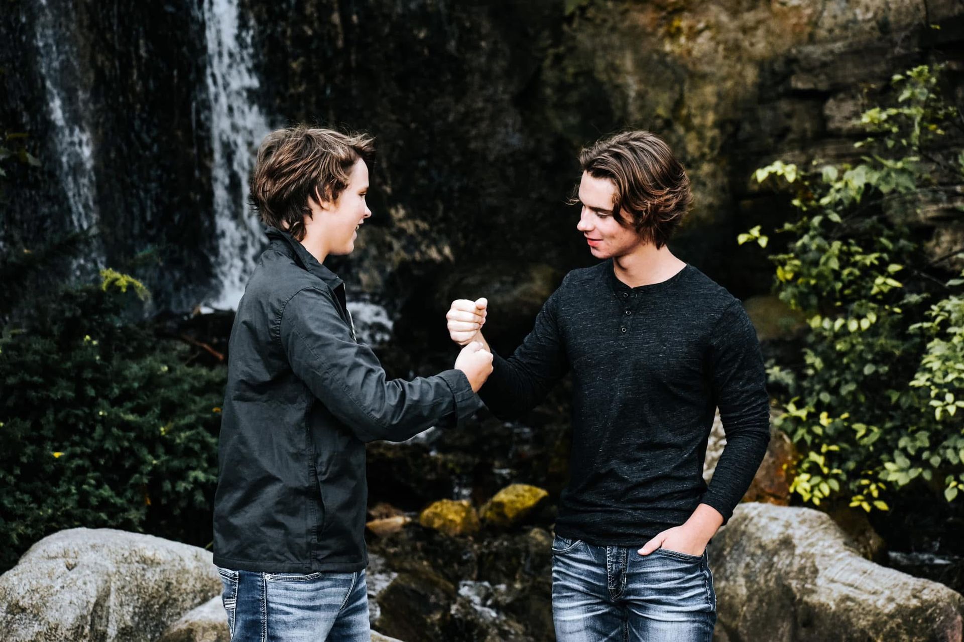 Two young men are shaking hands in front of a waterfall.