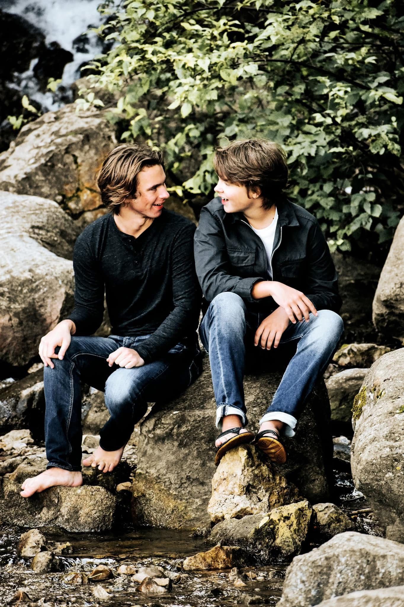 Two men are sitting on rocks near a stream talking to each other.