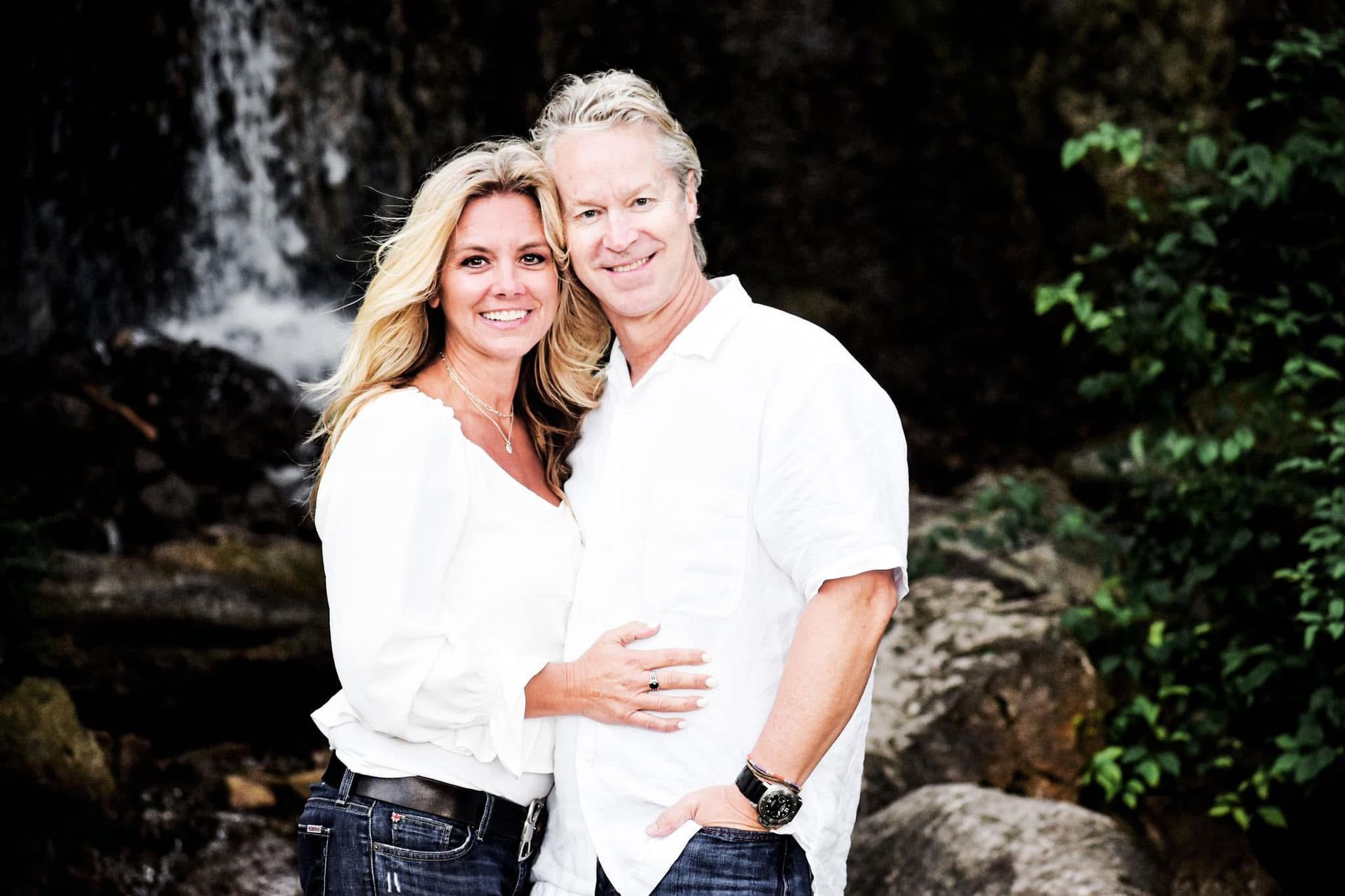 A man and a woman are posing for a picture in front of a waterfall.