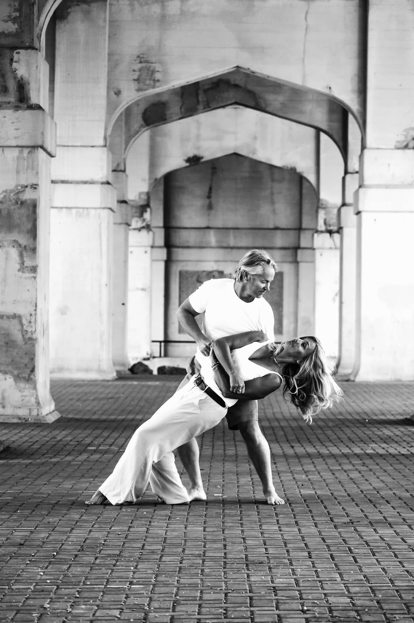 A black and white photo of two people dancing in front of a building.