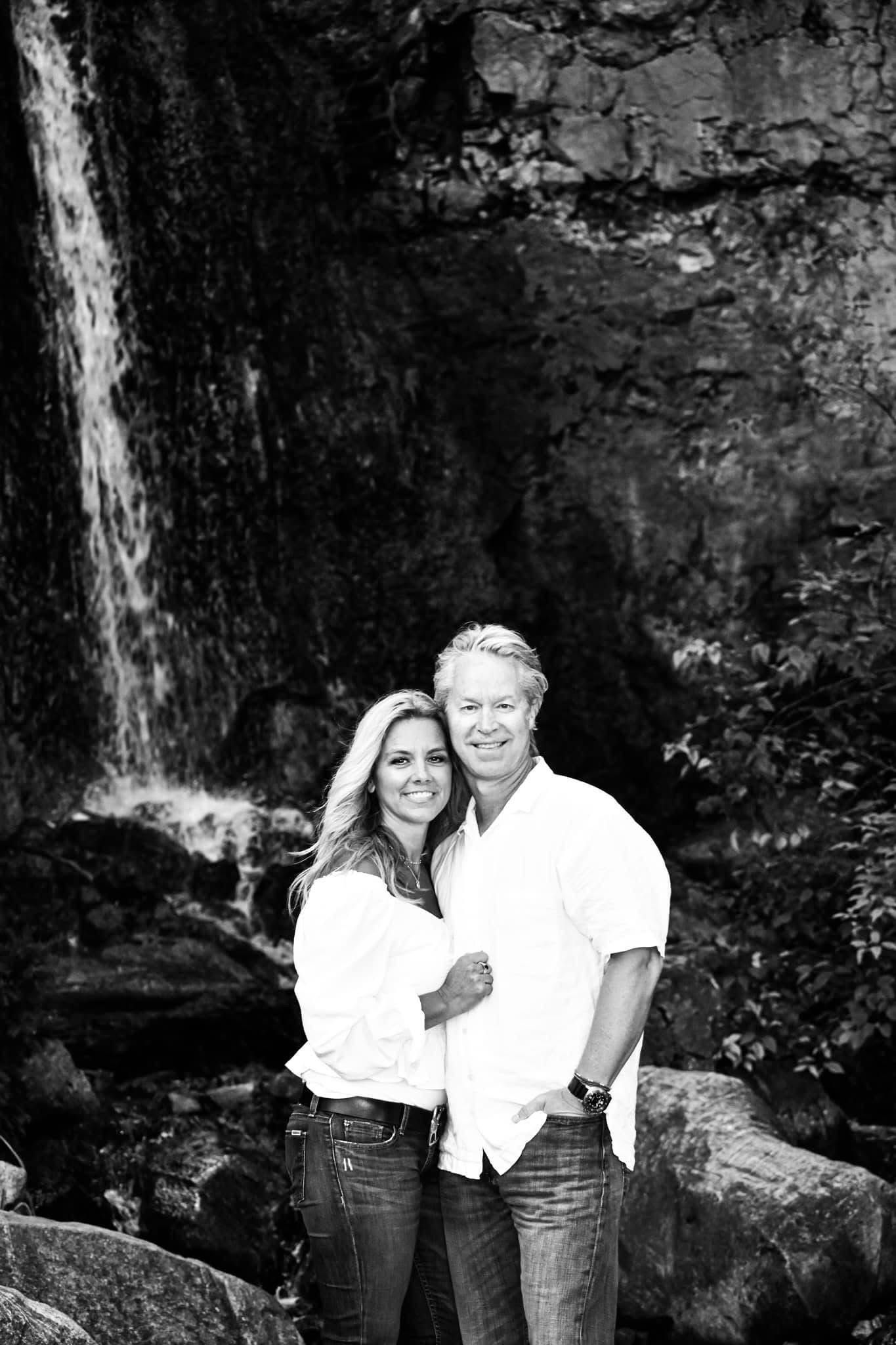 A black and white photo of a man and woman standing in front of a waterfall.