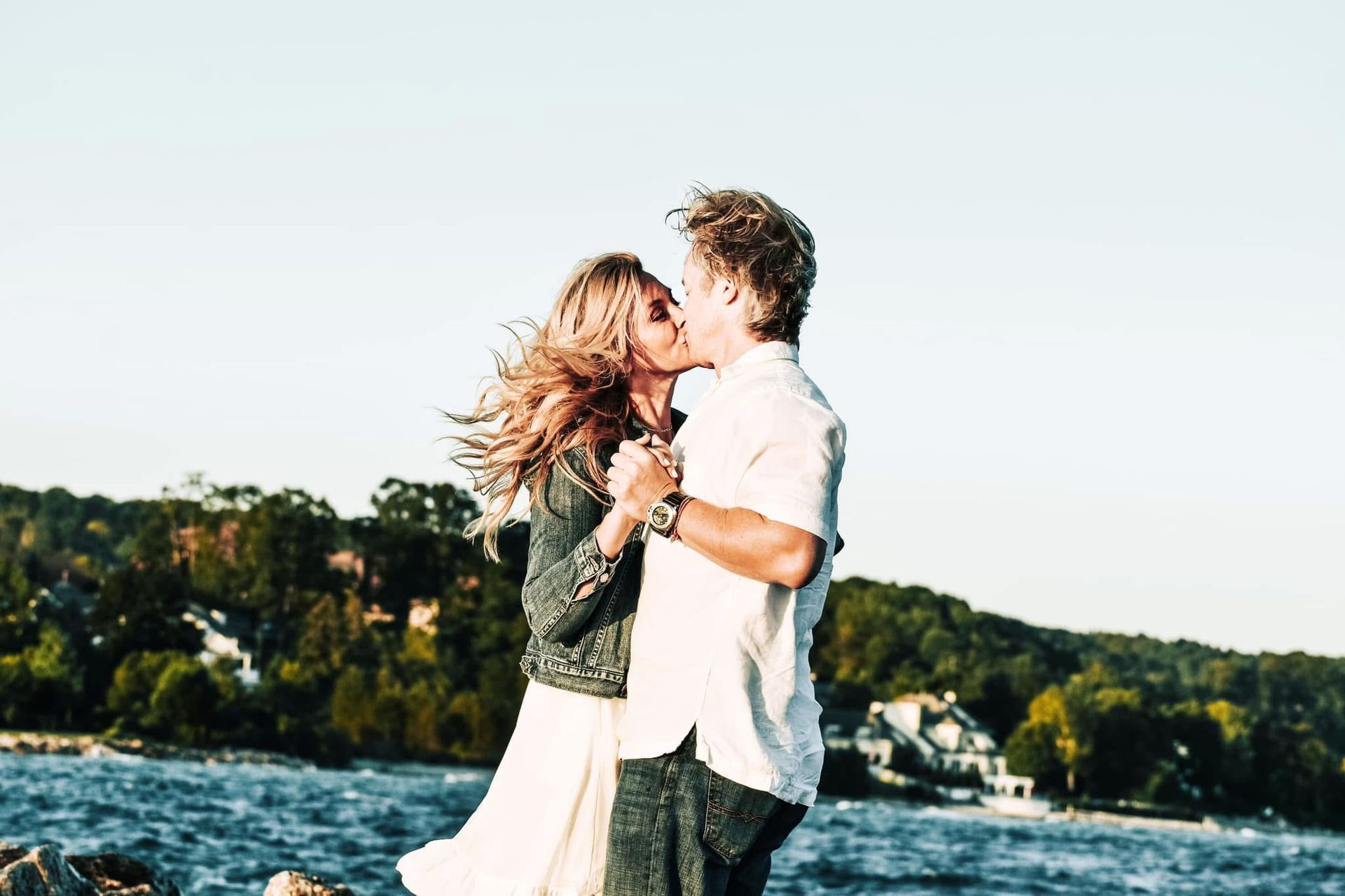 A man and a woman are kissing on the shore of a lake.