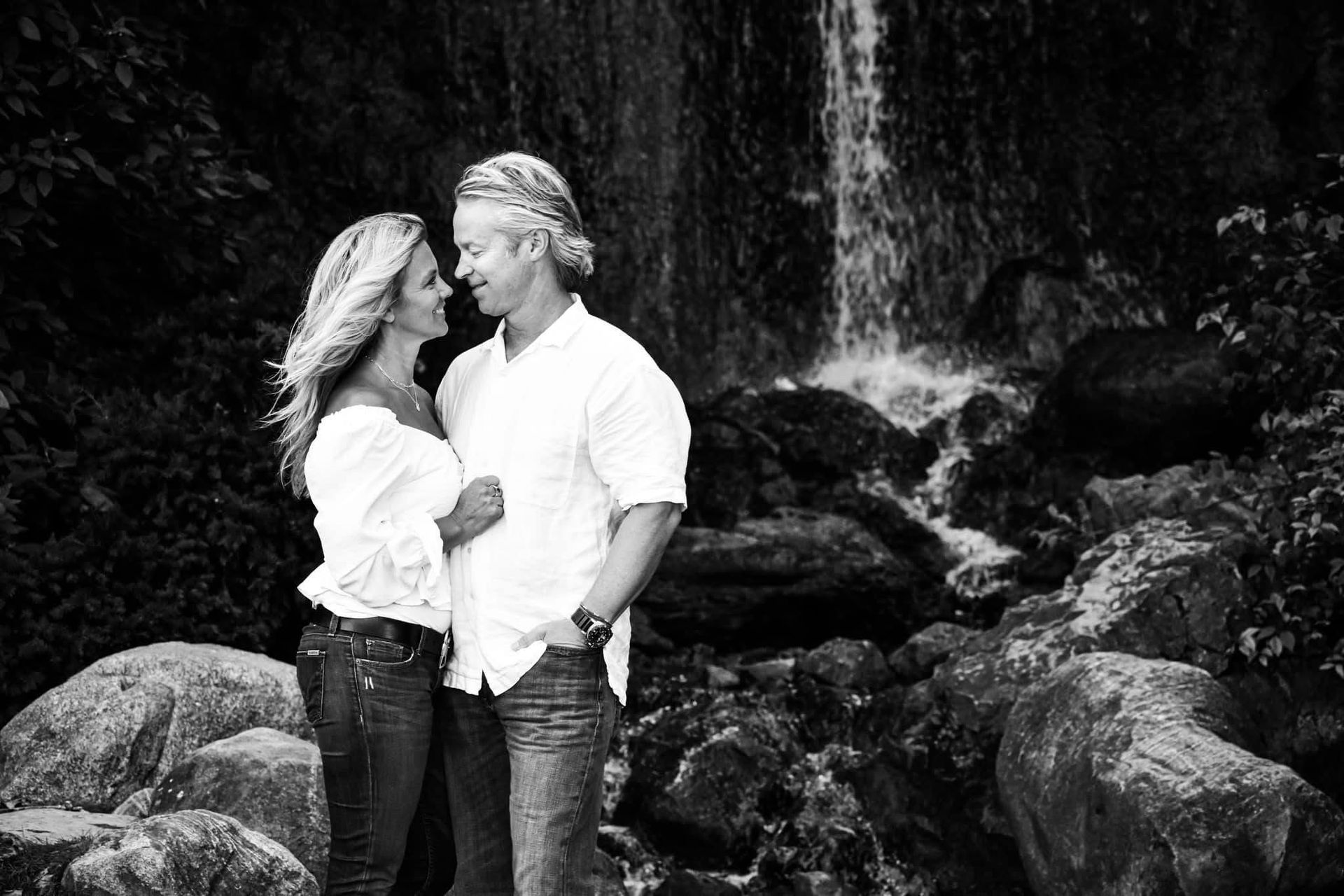 A black and white photo of a man and woman standing in front of a waterfall.