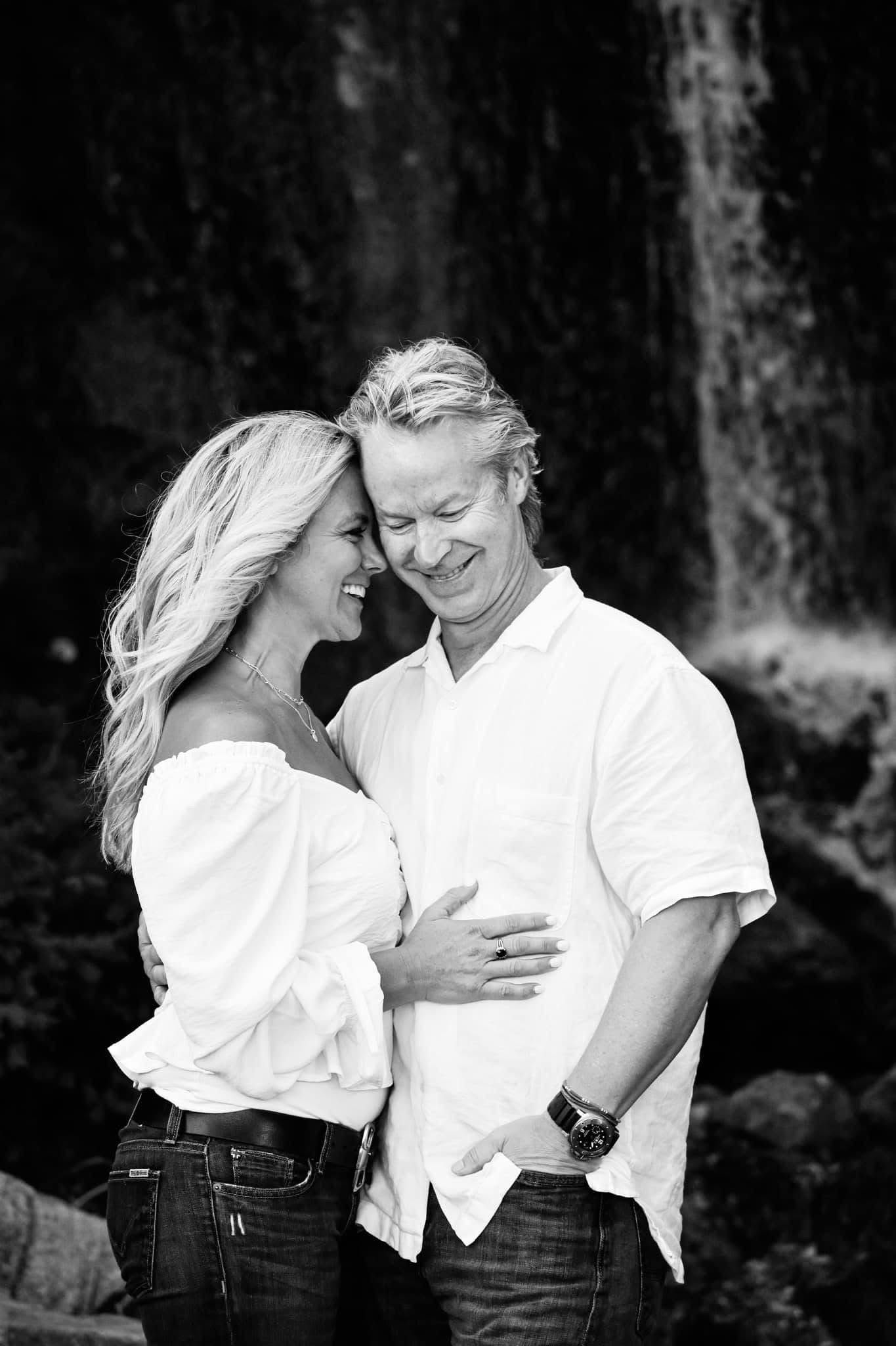 A man and a woman are standing next to each other in front of a waterfall.