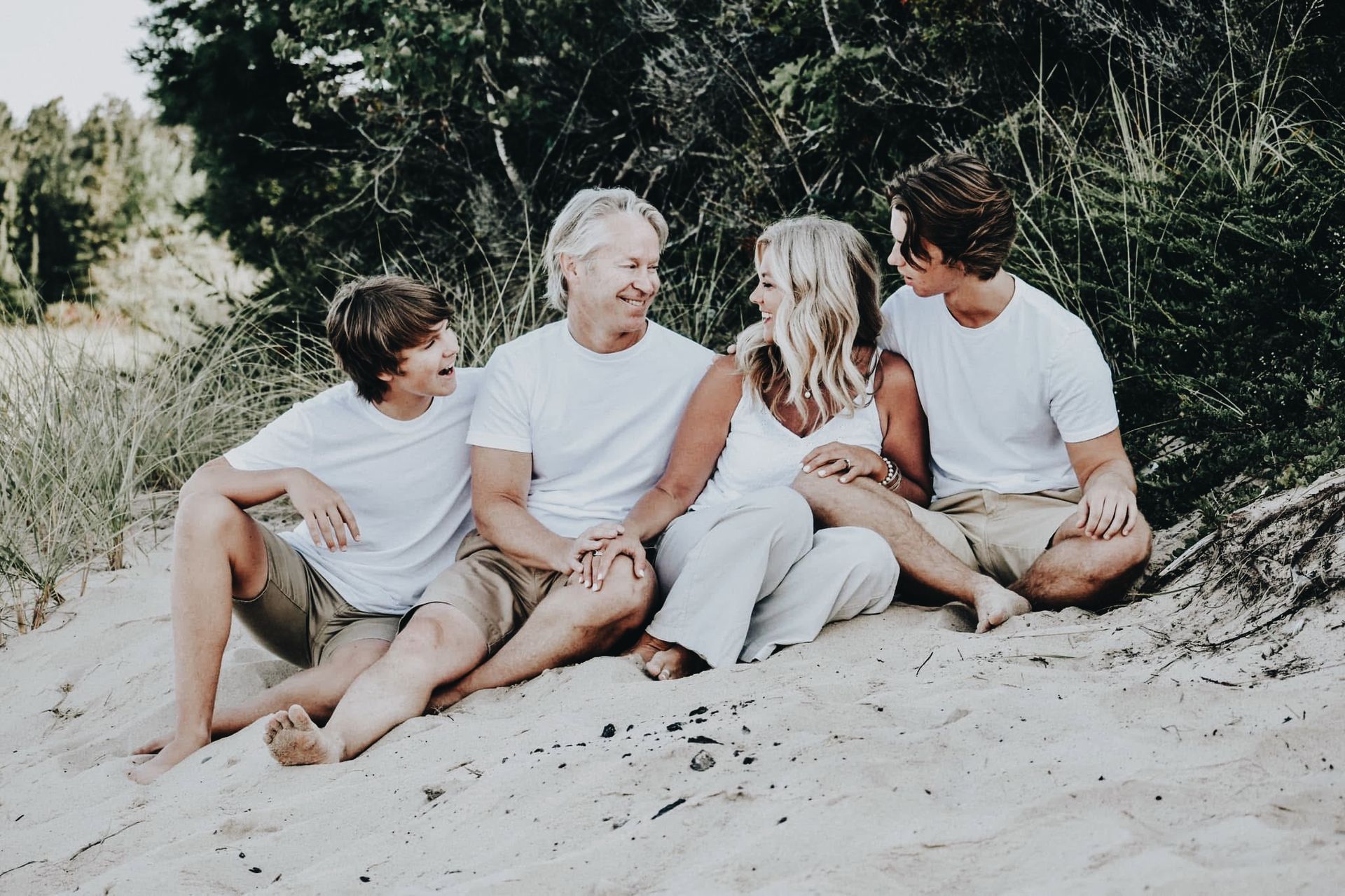 A family is sitting on a sand dune wearing white shirts