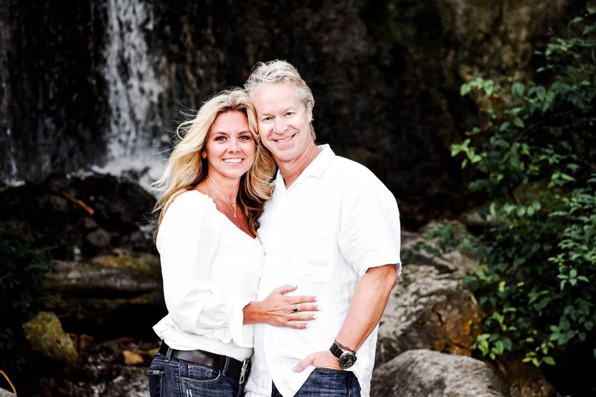 A man and a woman are posing for a picture in front of a waterfall.