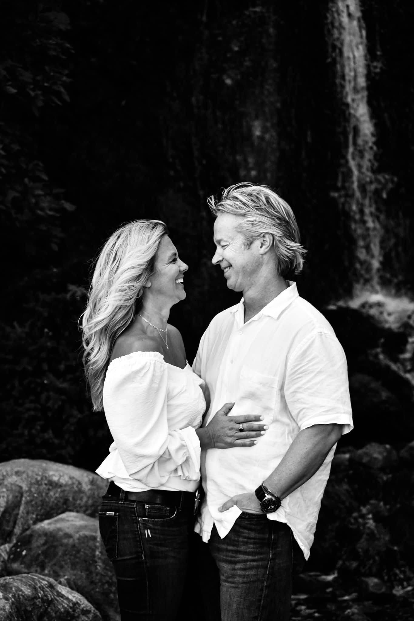A man and a woman are standing next to each other in front of a waterfall.