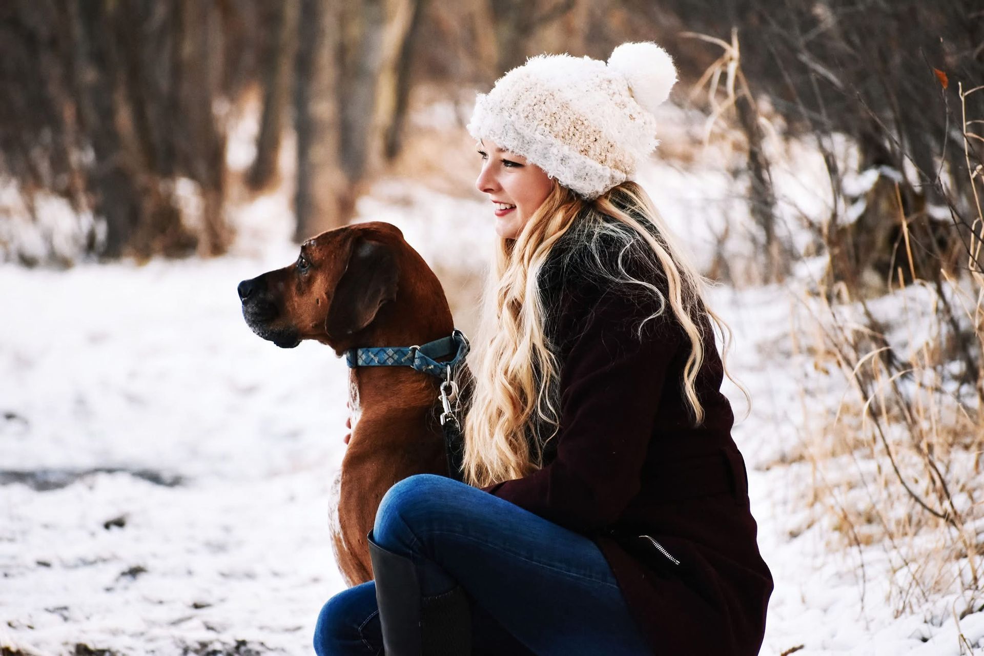 A woman is kneeling down next to a brown dog in the snow.