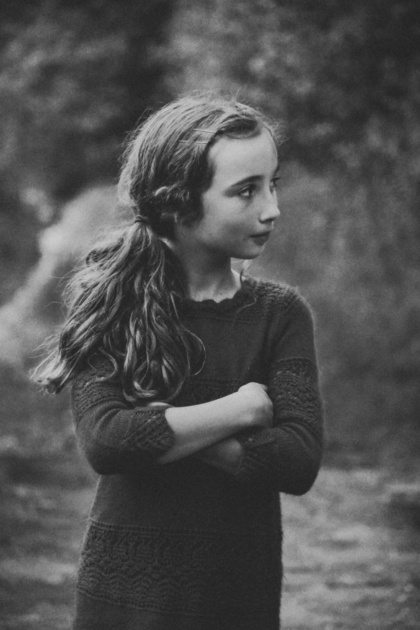 A black and white photo of a young girl with her arms crossed.