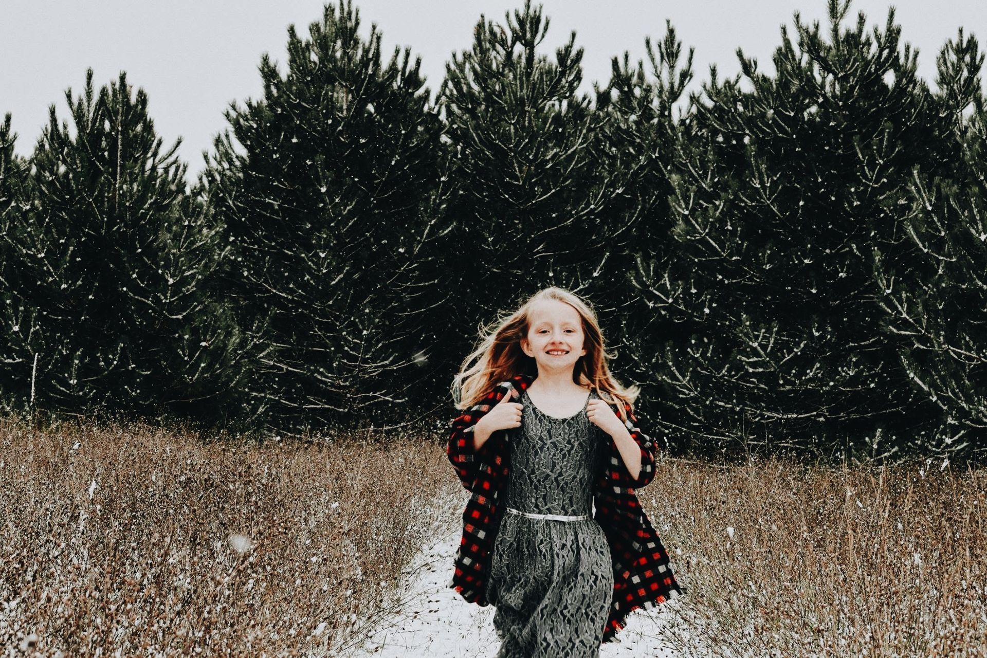 A little girl is running in a field with trees in the background.