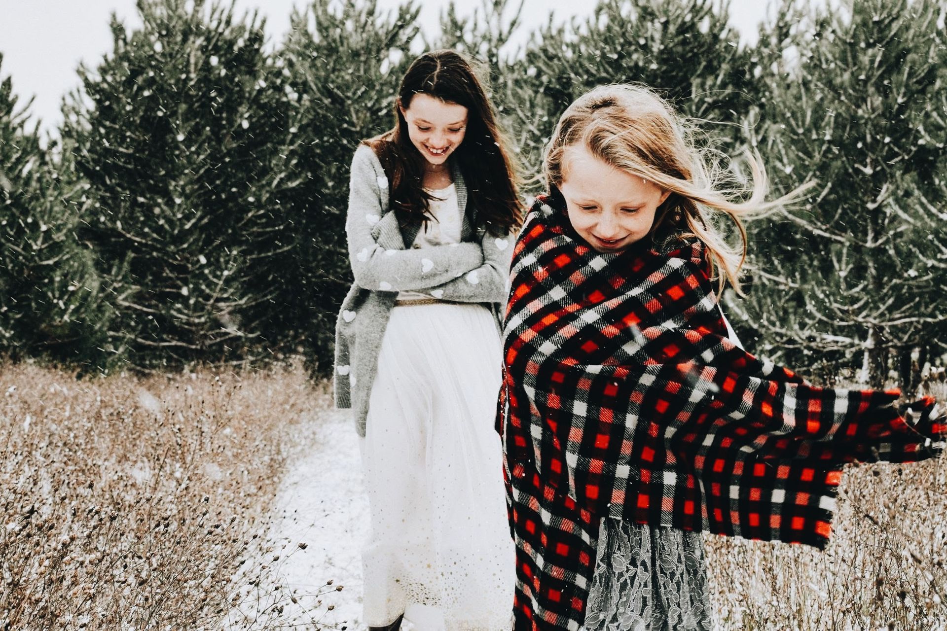 Two girls are standing in a snowy field . one girl is wrapped in a plaid scarf.