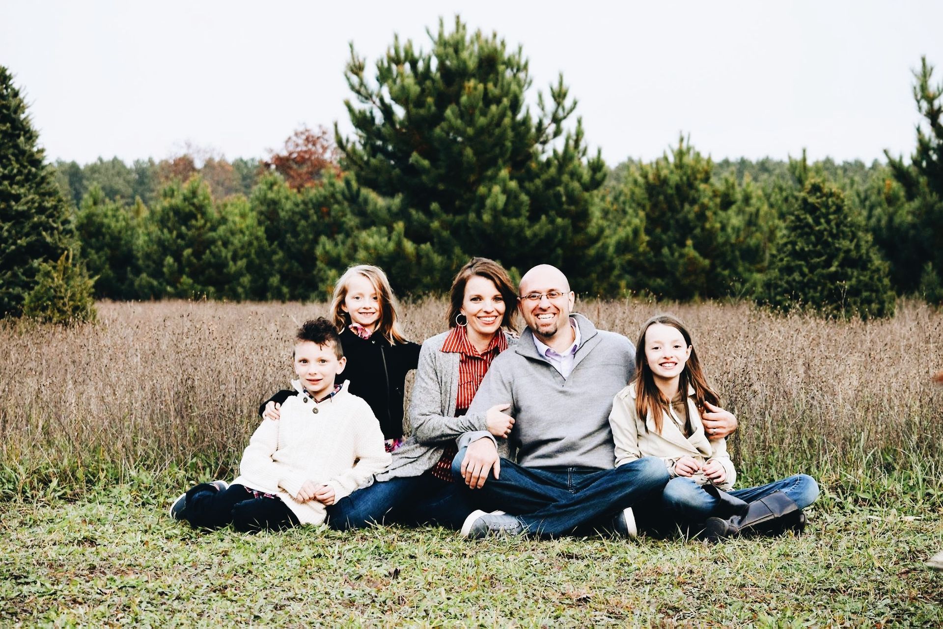 A family is posing for a picture while sitting on the grass in a field.