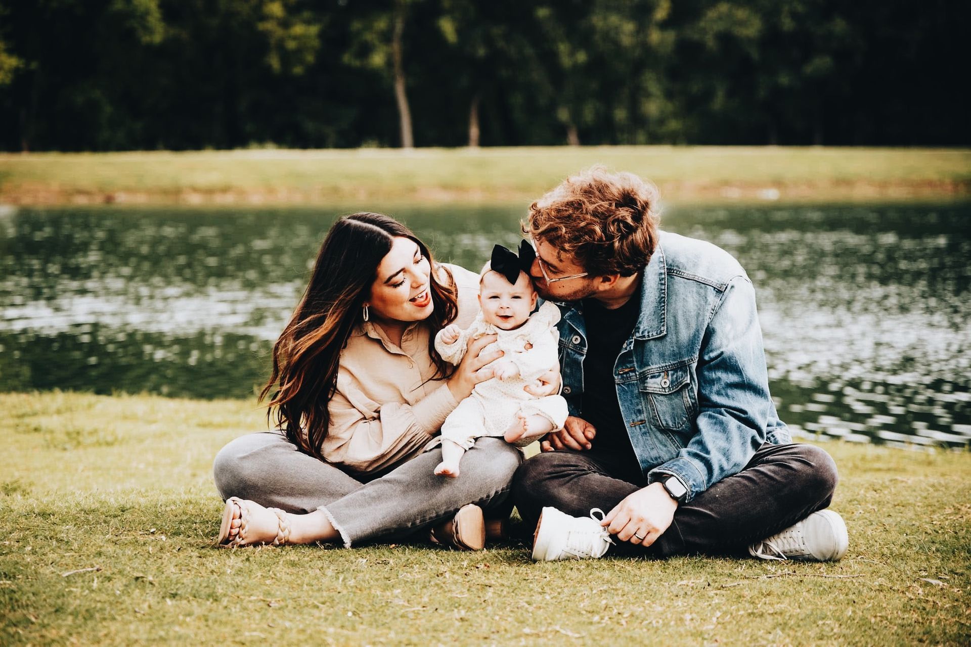 A man and woman are sitting on the grass holding a baby.