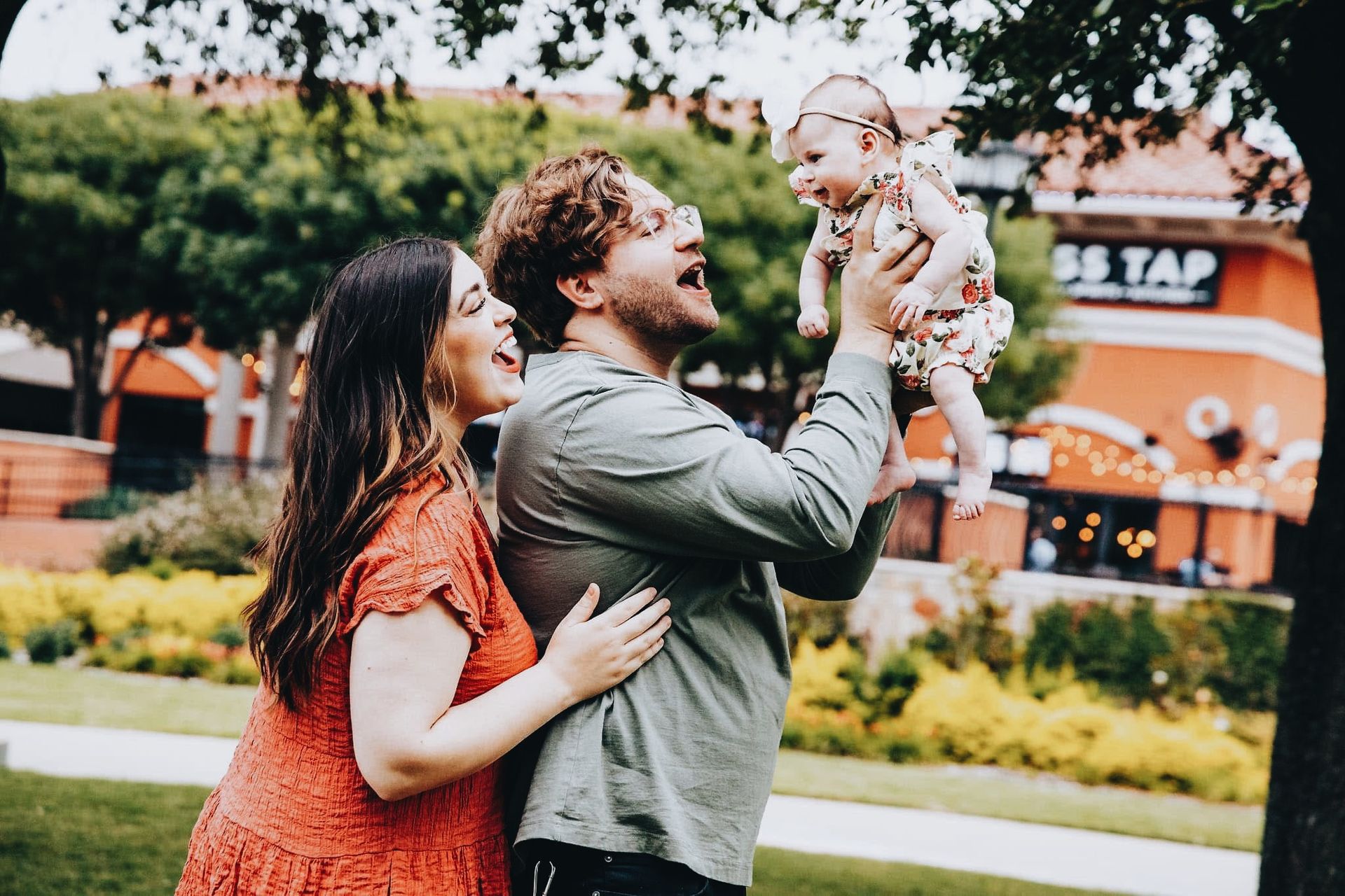 A man and woman are holding a baby in their arms in a park.