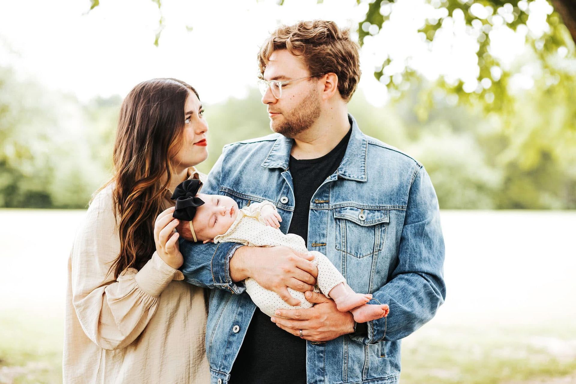 A man and a woman are holding a baby in a park.