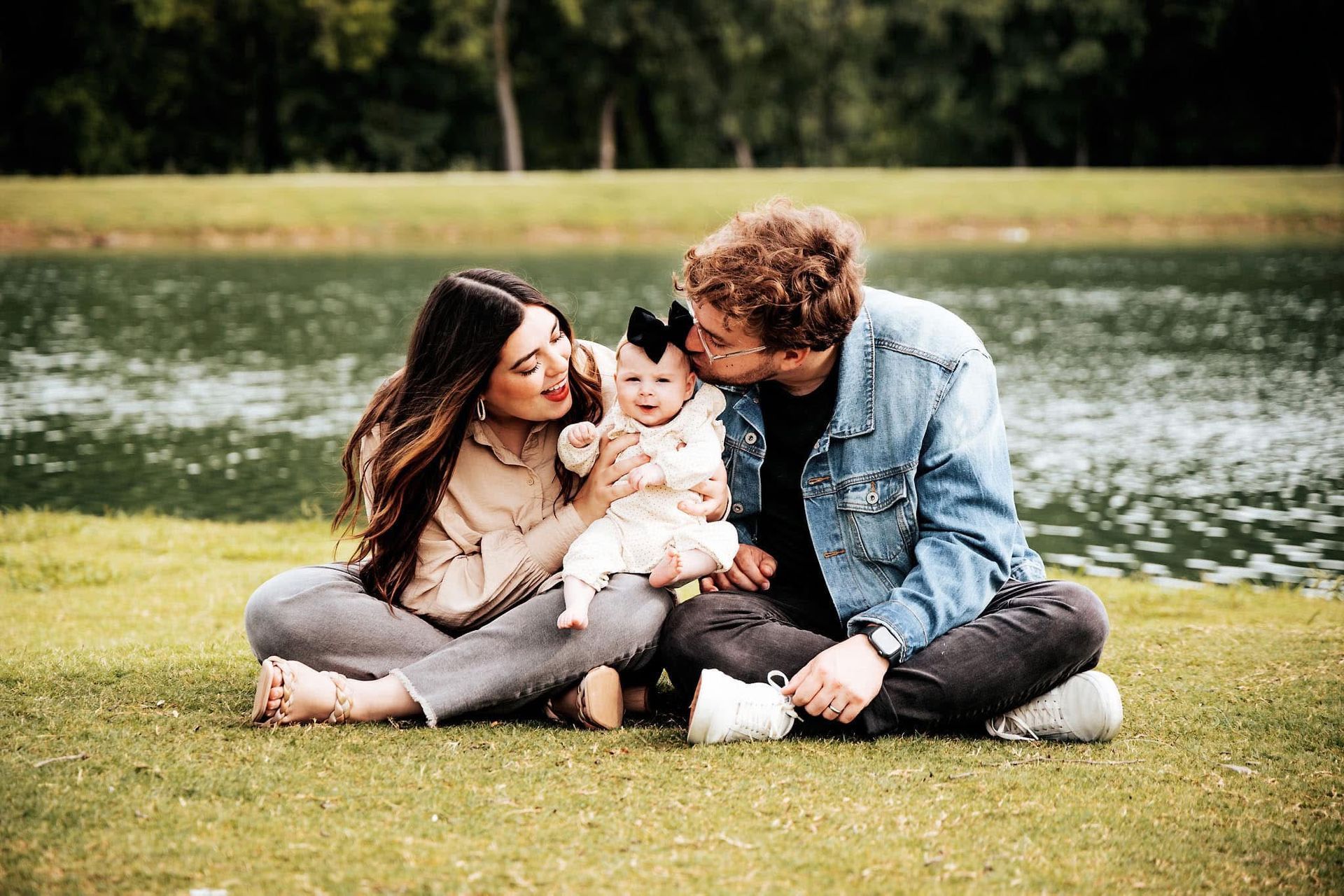 A man and woman are sitting on the grass holding a baby.