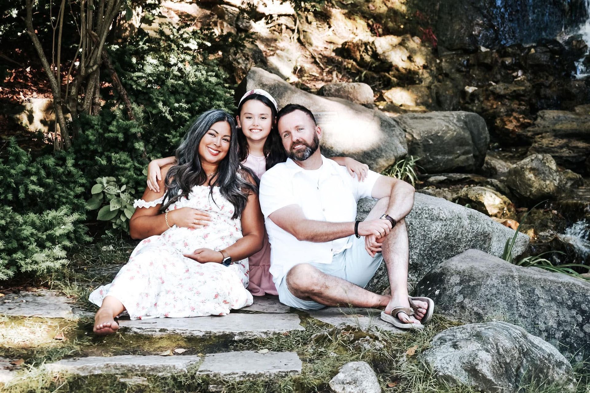 A man and two women are sitting on steps next to a waterfall.