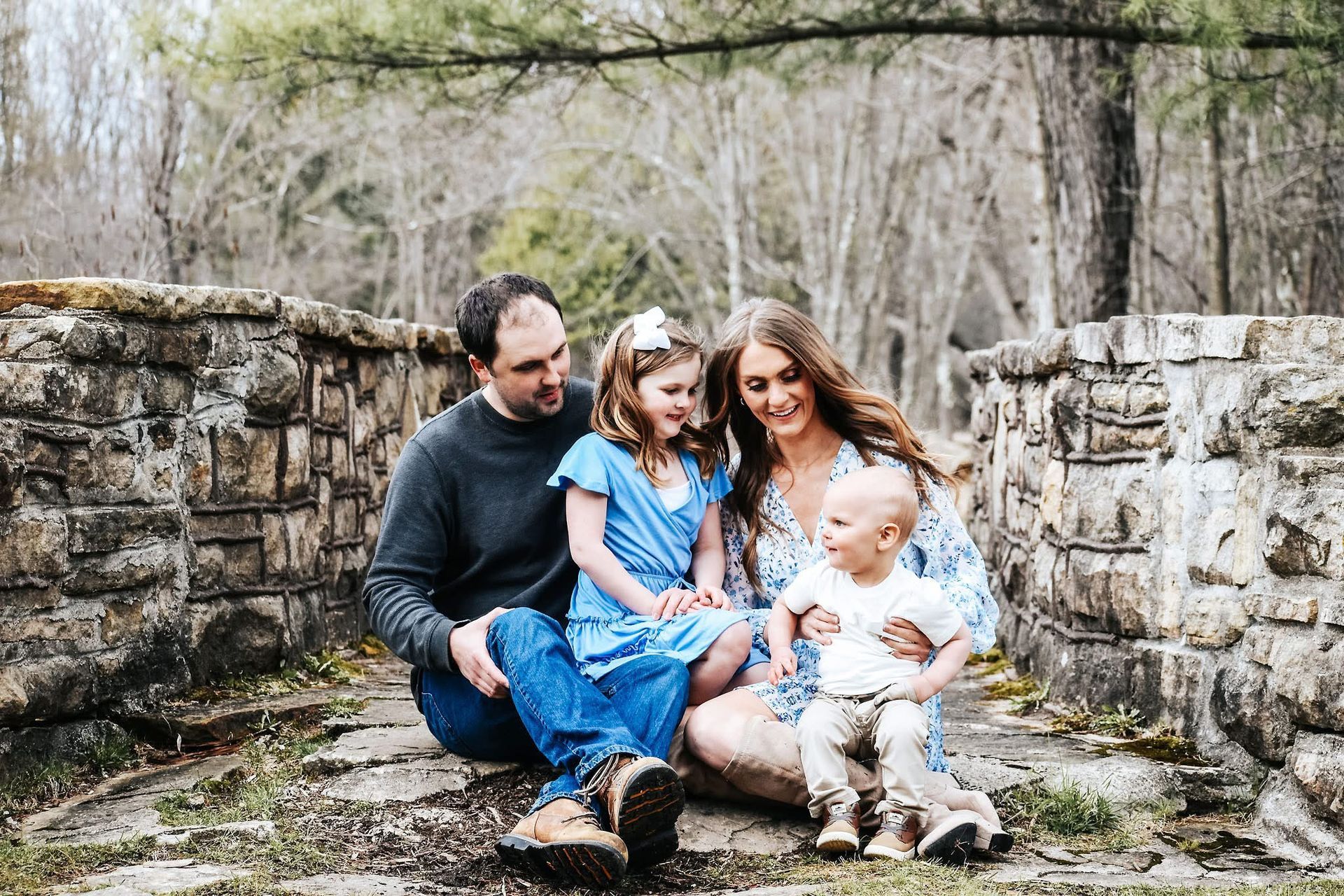 A family is sitting on a rock in front of a stone wall.