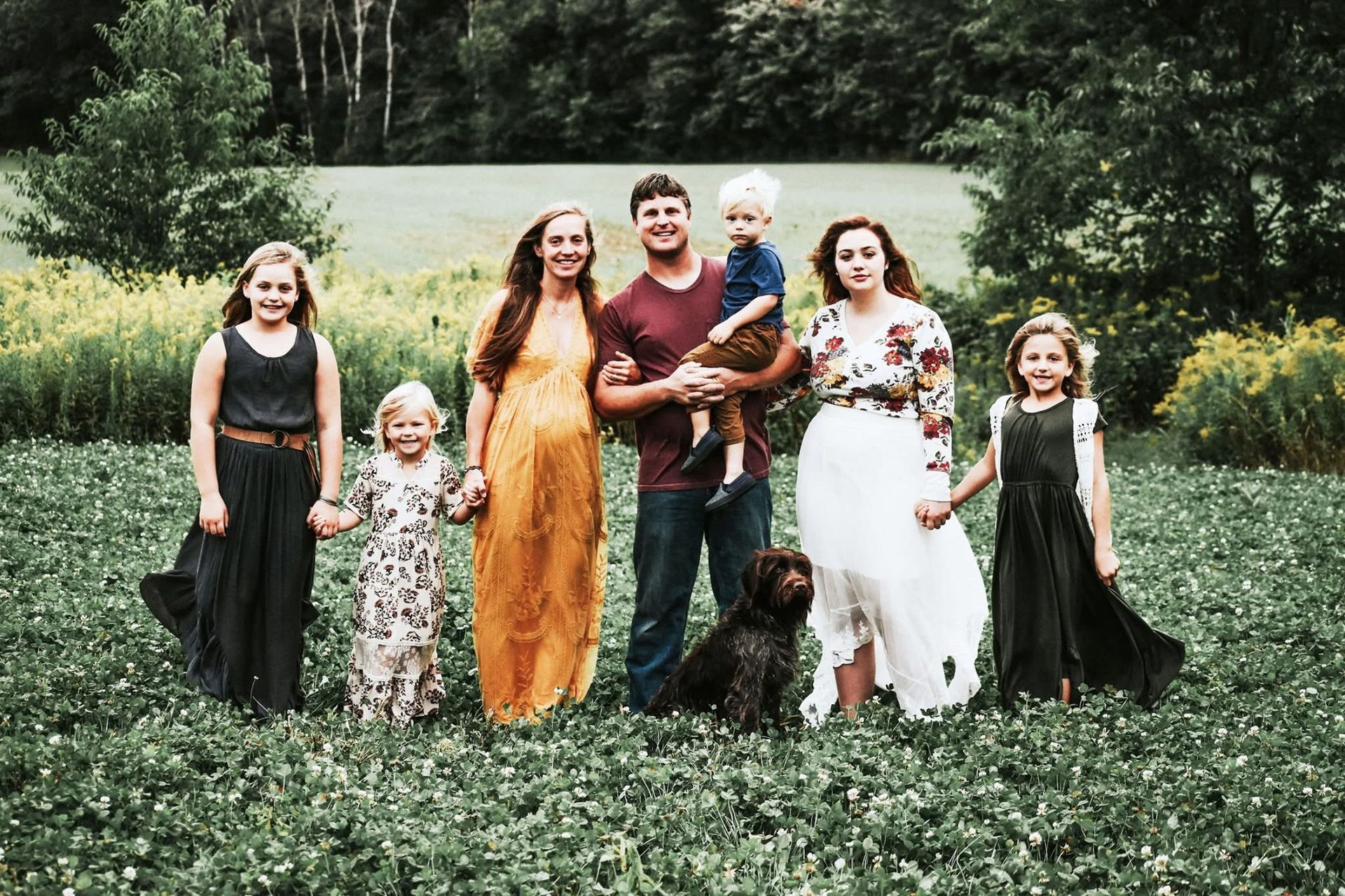 A family is posing for a picture in a field with a dog.