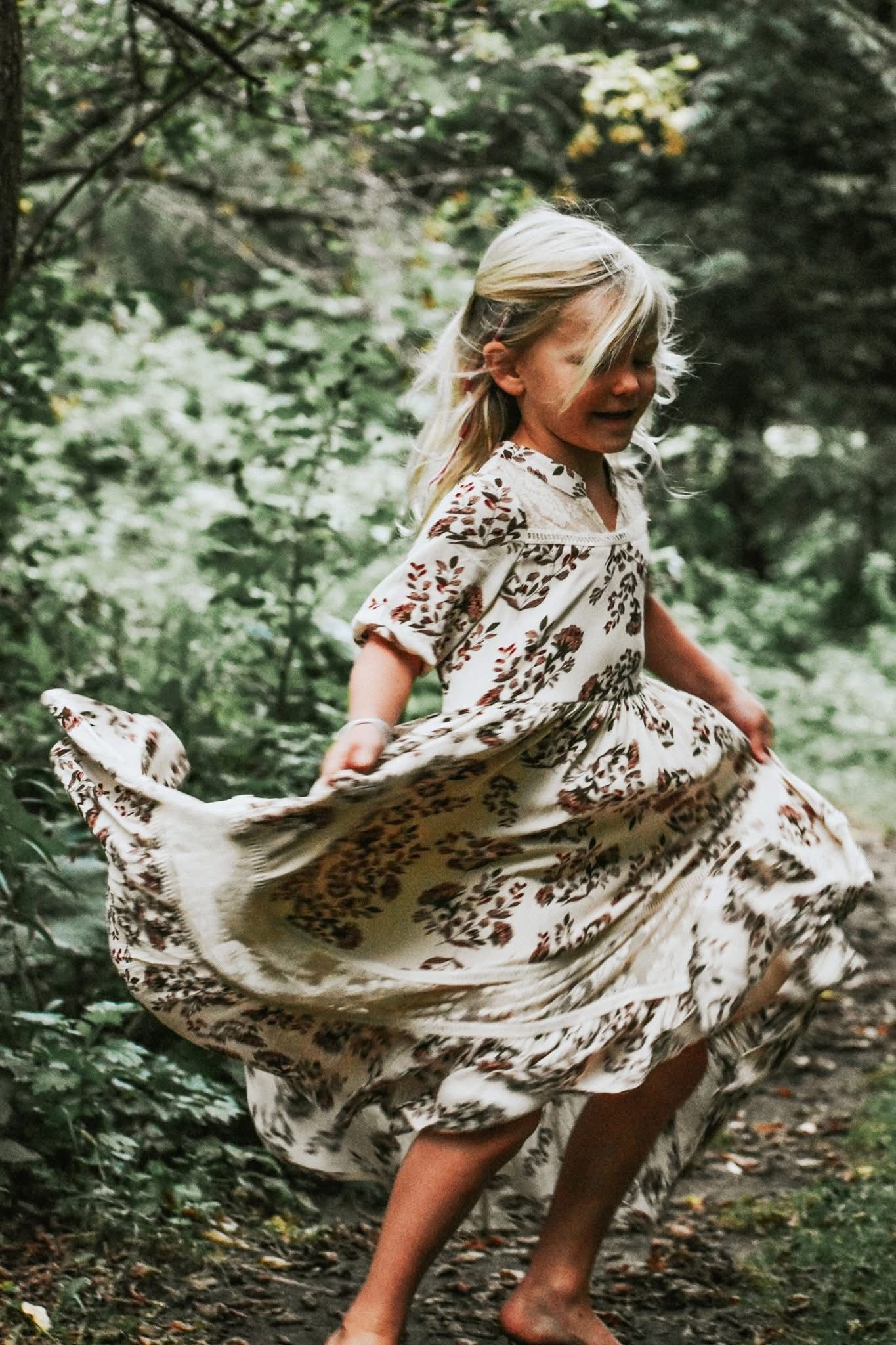 A little girl in a dress is dancing in the woods.