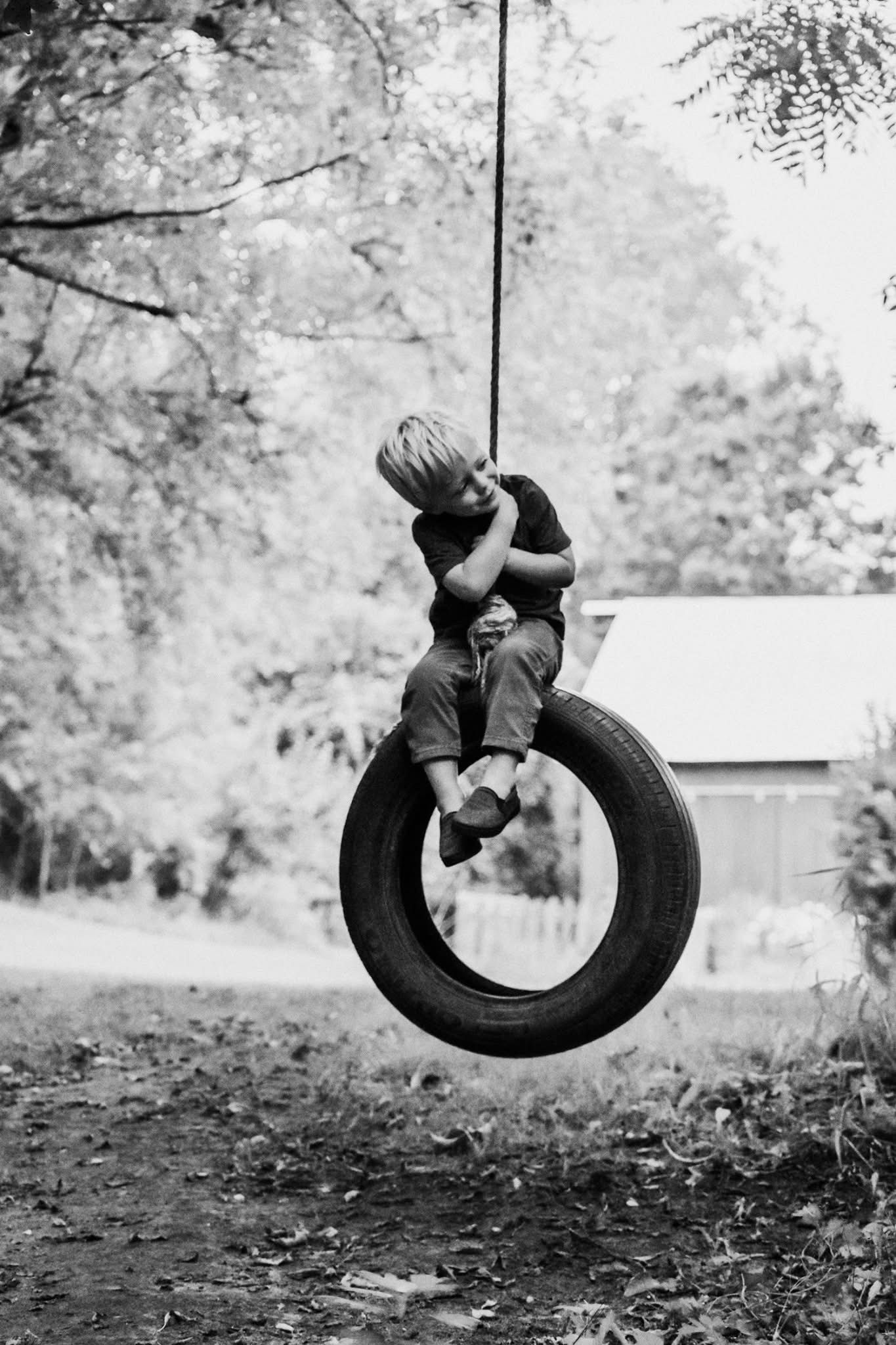 A young boy is sitting on a tire swing.