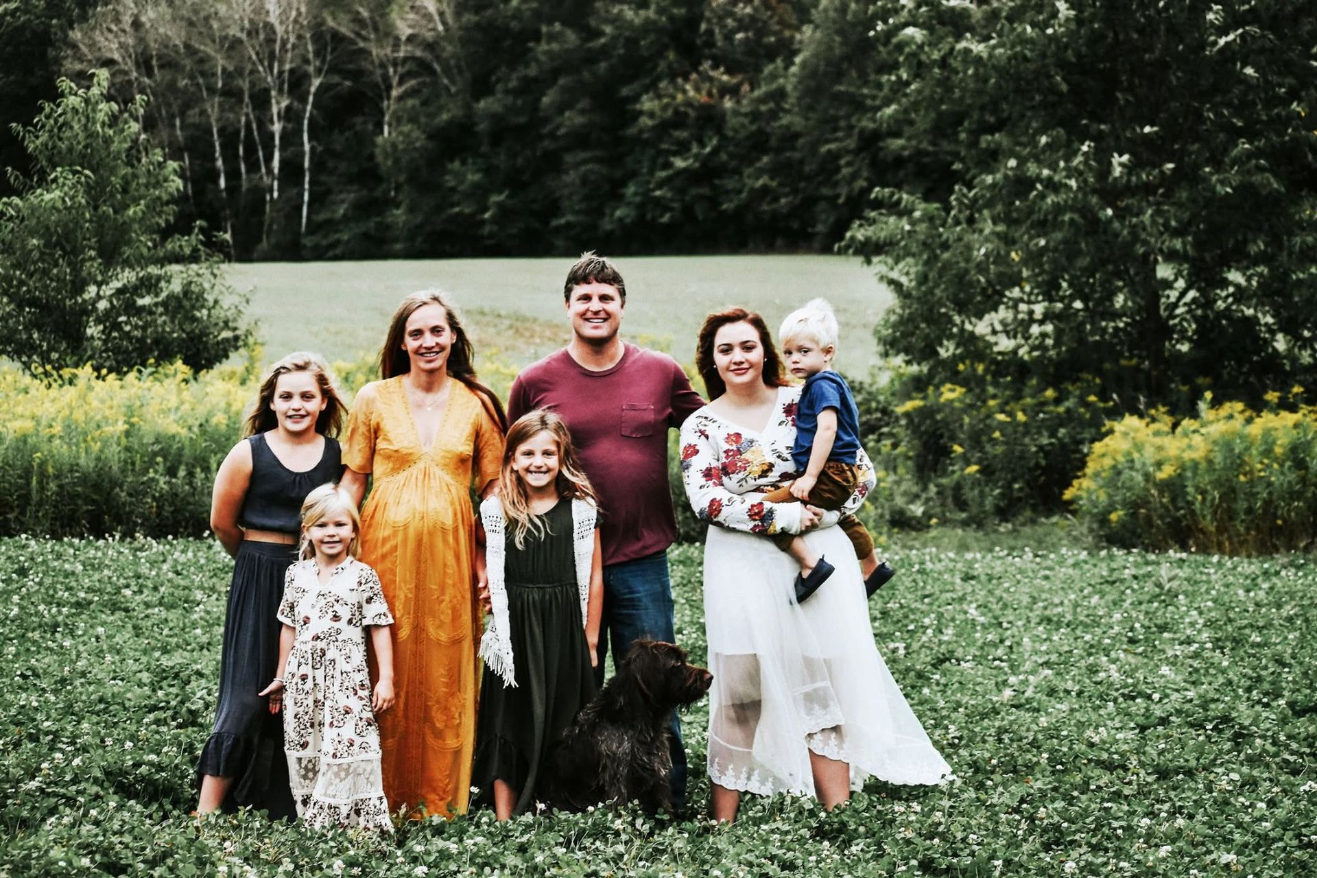 A family posing for a picture in a field with a dog.