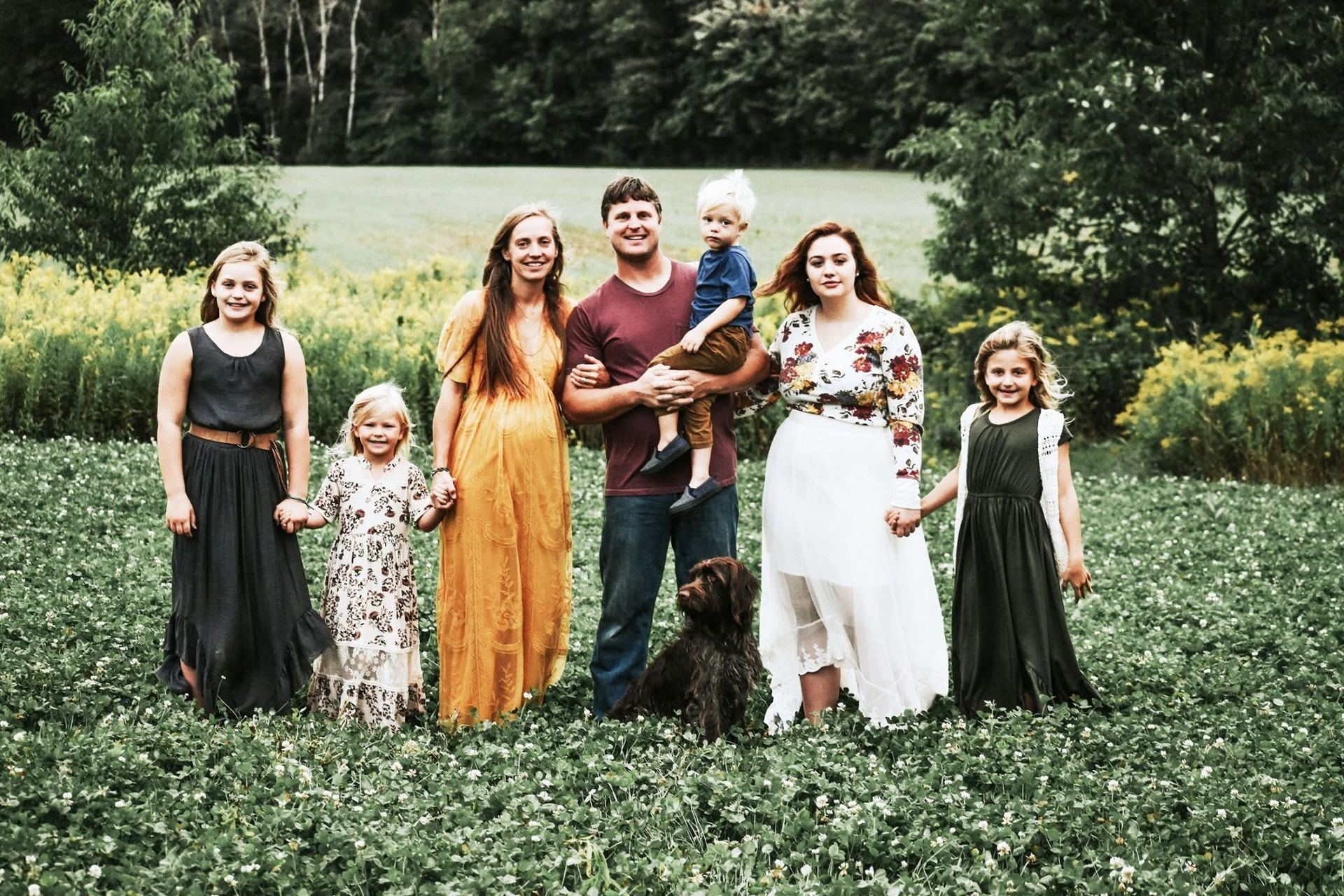 A family is posing for a picture in a field with a dog.
