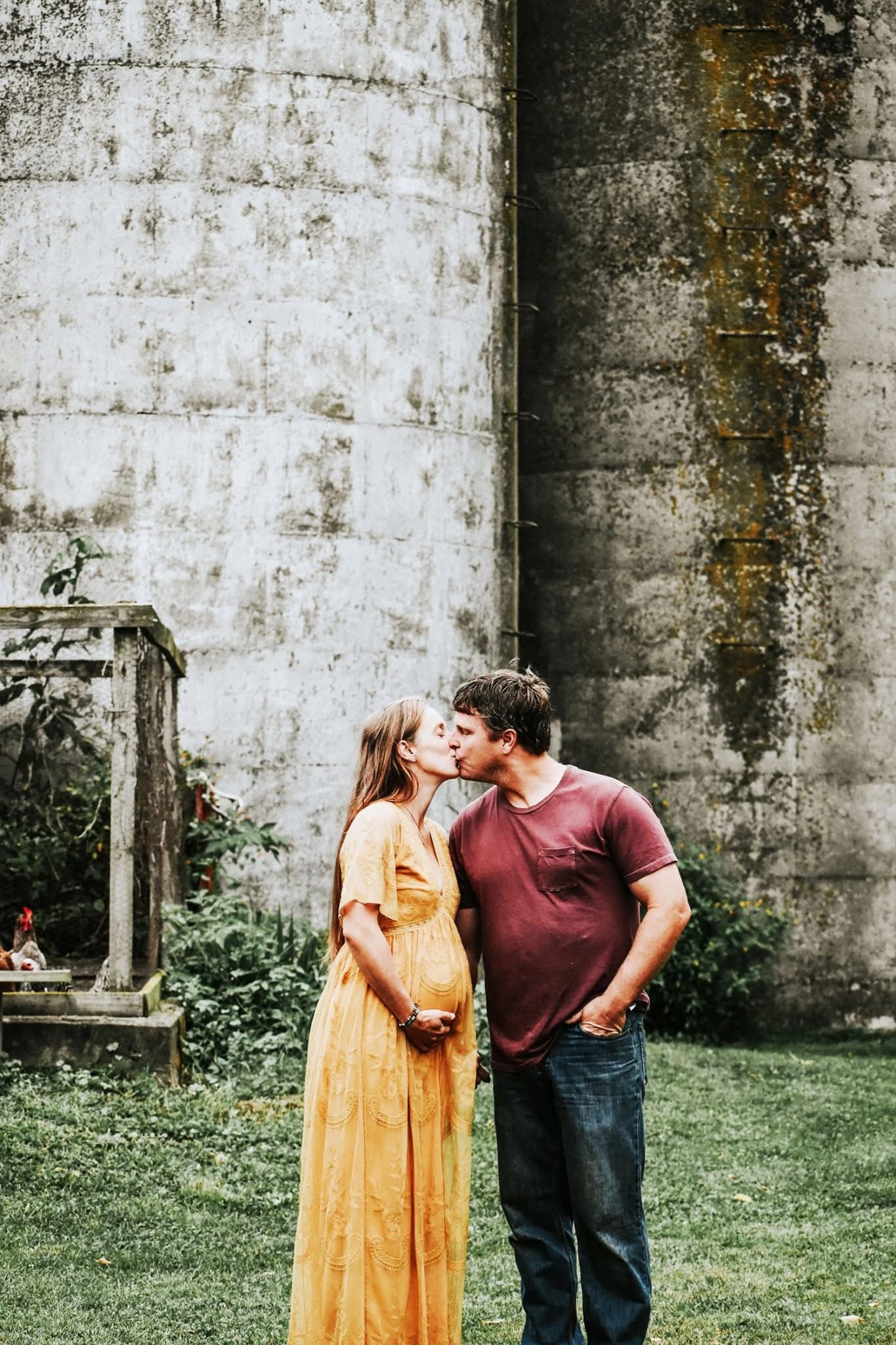 A man and a pregnant woman are kissing in front of a building.