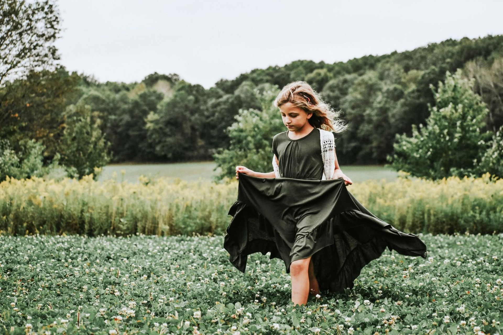 A little girl in a black dress is standing in a field.