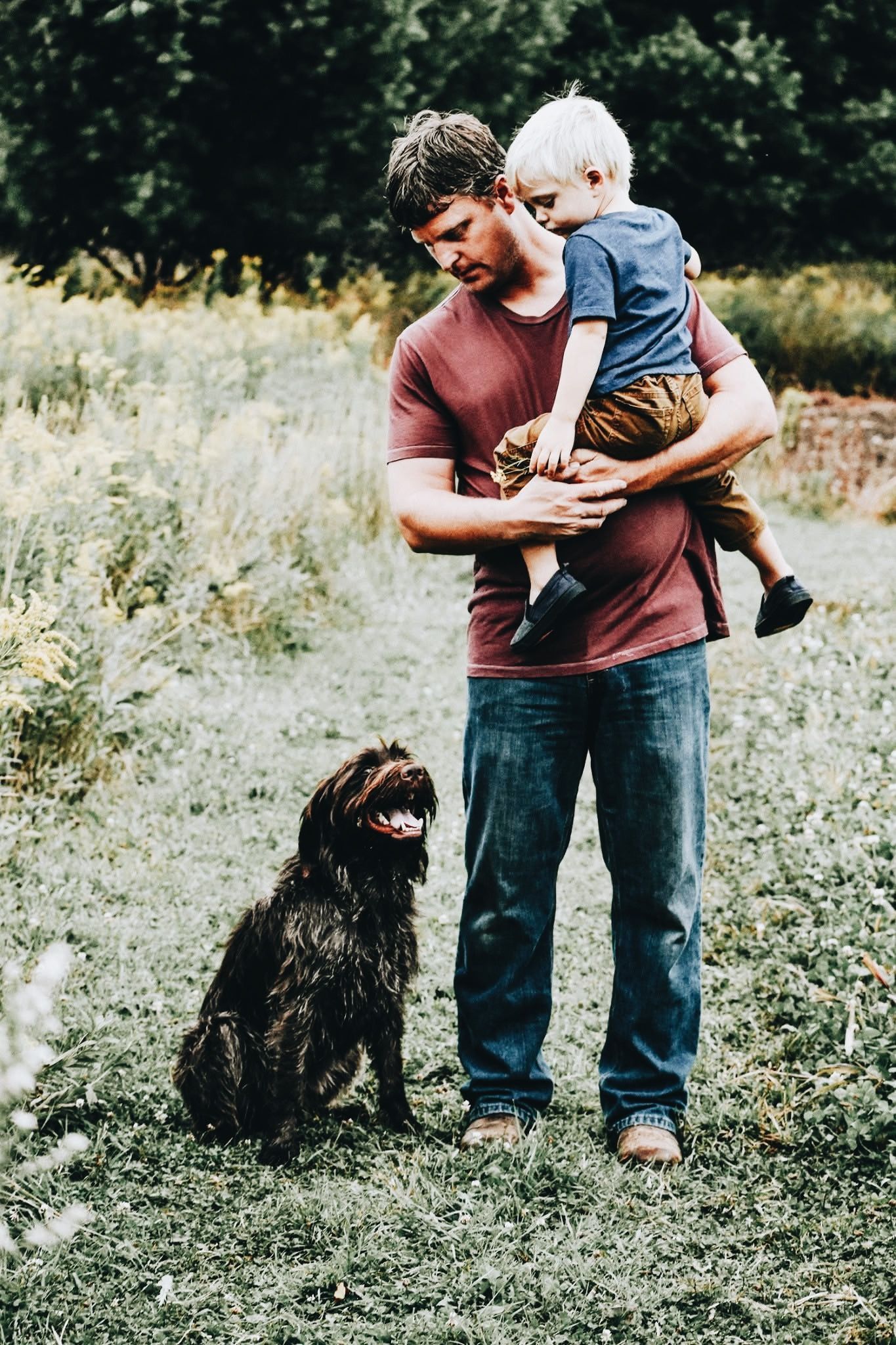 A man holding a child and a dog in a field