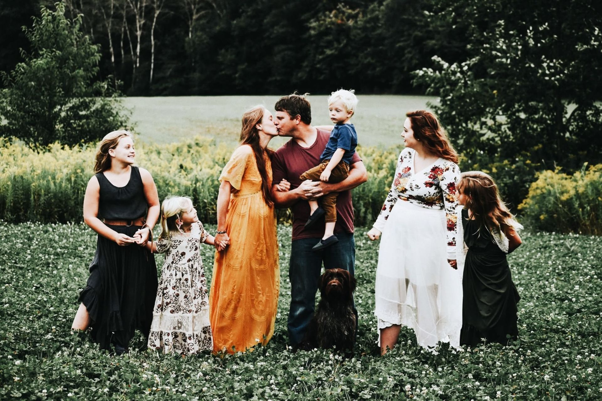 A family is posing for a picture in a field with a dog.