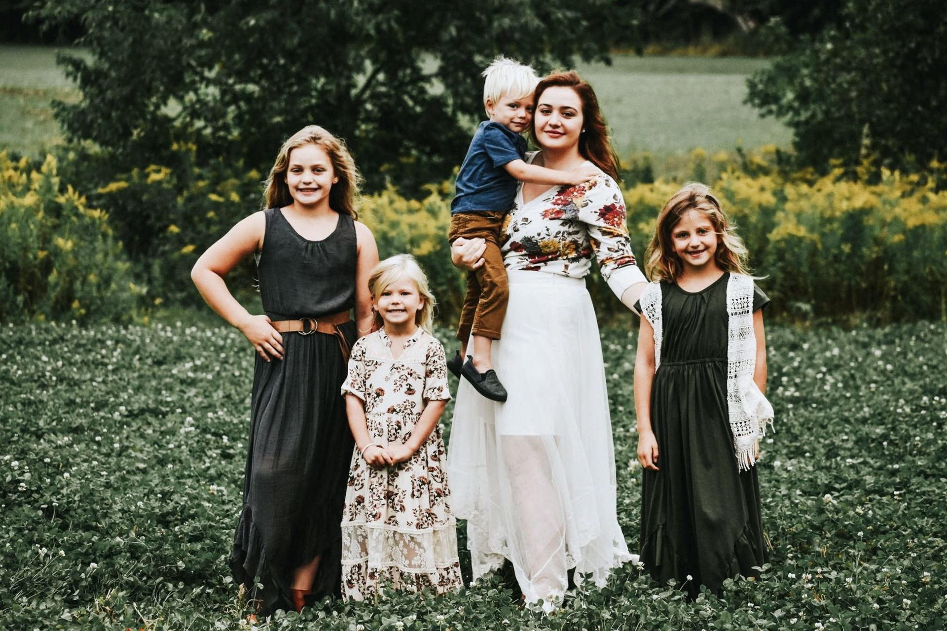 A woman is standing in a field with three children.